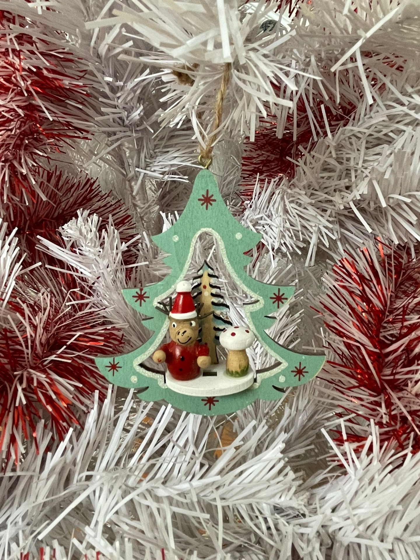 Enfeite natalício de madeira em árvore verde com boneco e coelho pendurado em árvore branca com detalhes vermelhos