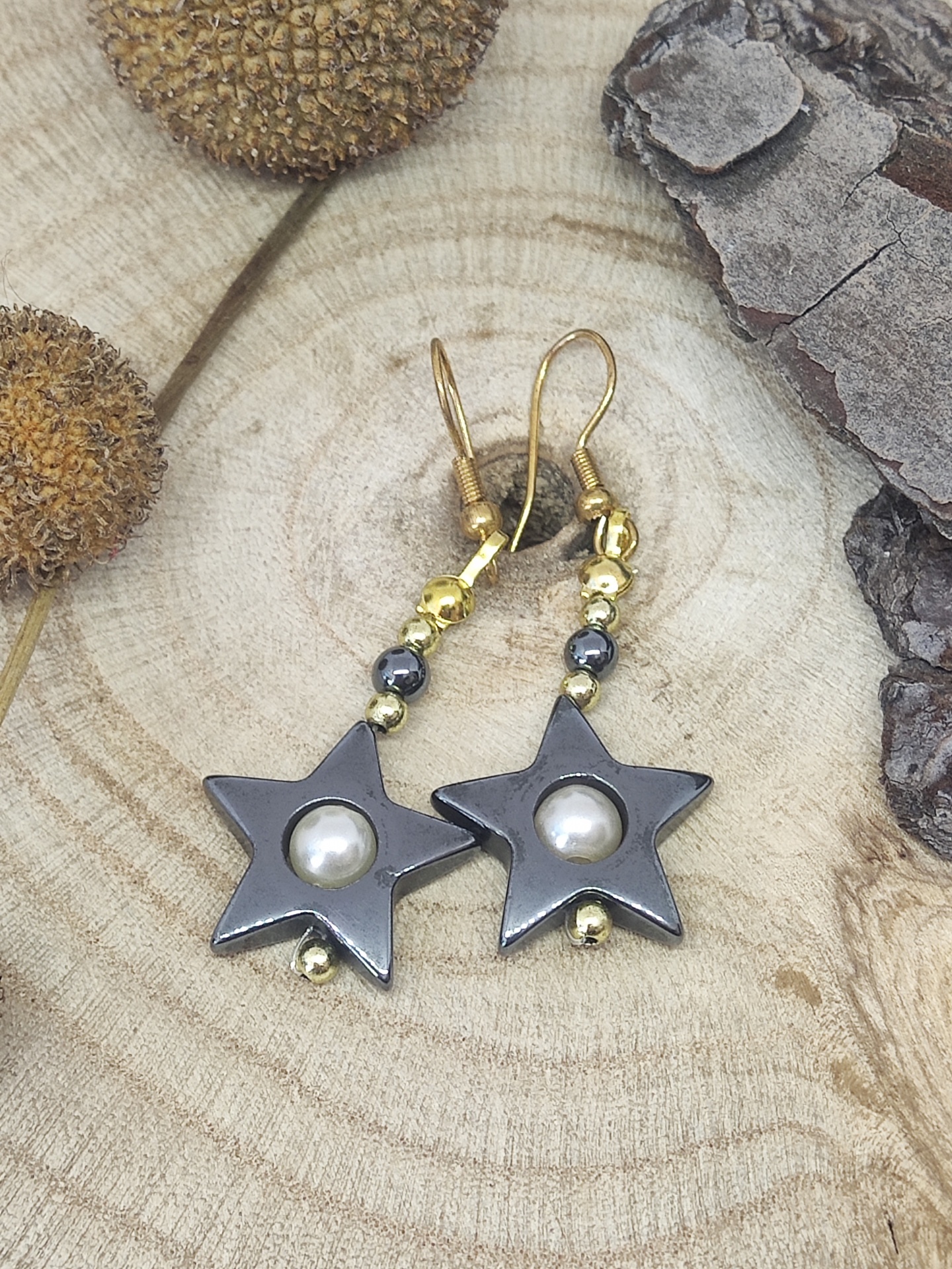 Brincos estrela cinza com pérola e contas douradas sobre madeira