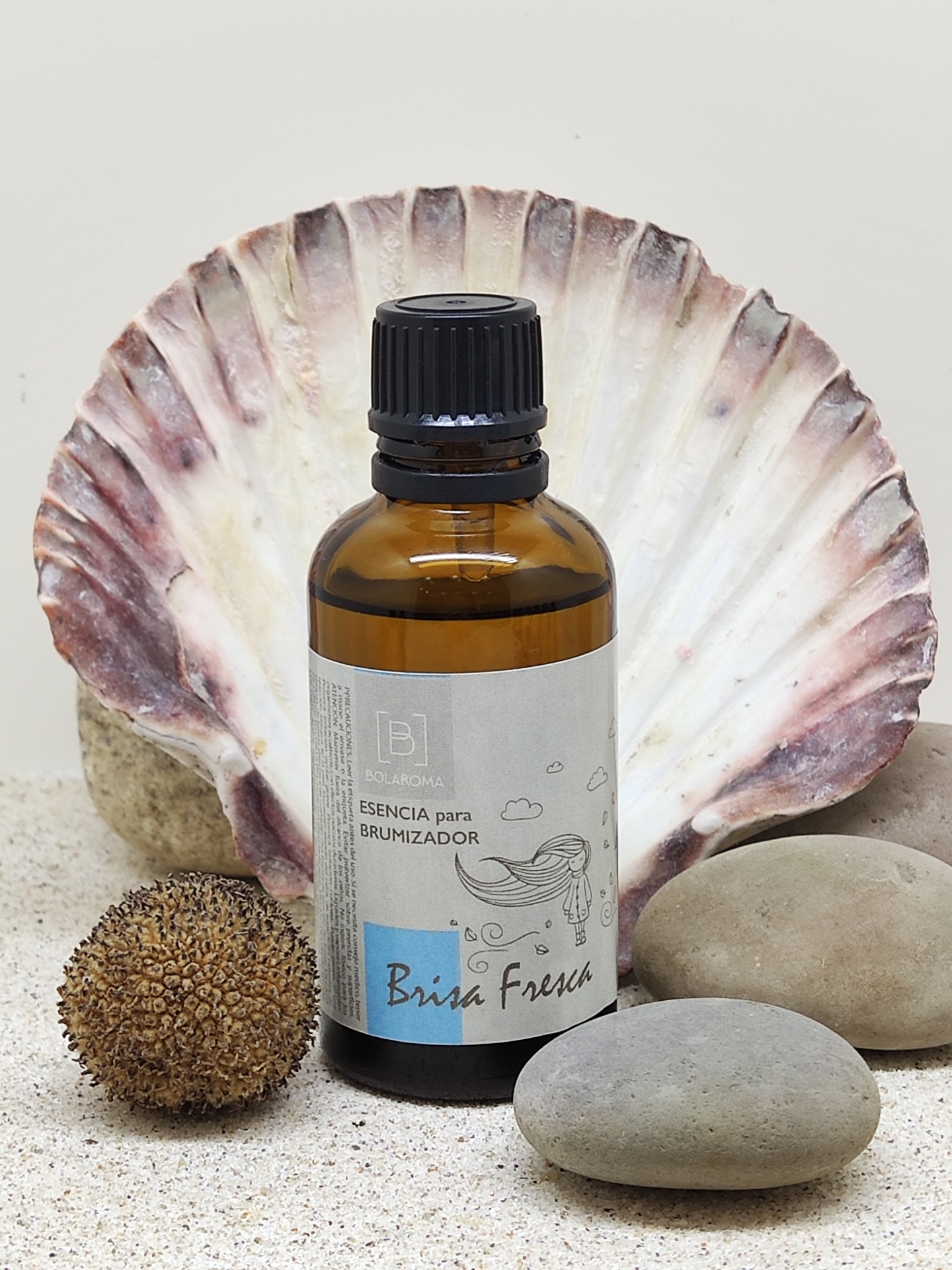 Frasco de essência para brumizador Brisa Fresca junto a pedras e concha na areia