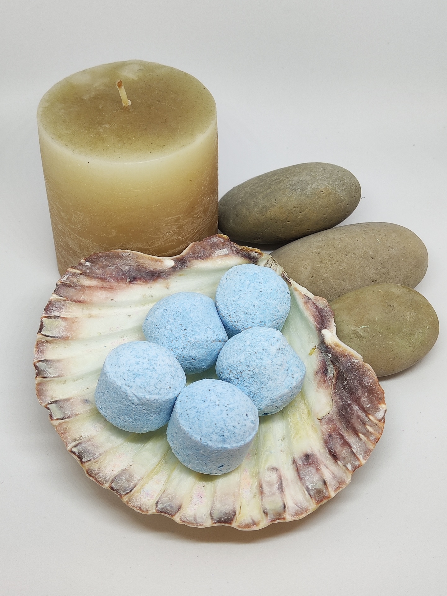 Pastilhas azuis em concha natural com vela amarela e pedras cinzentas
