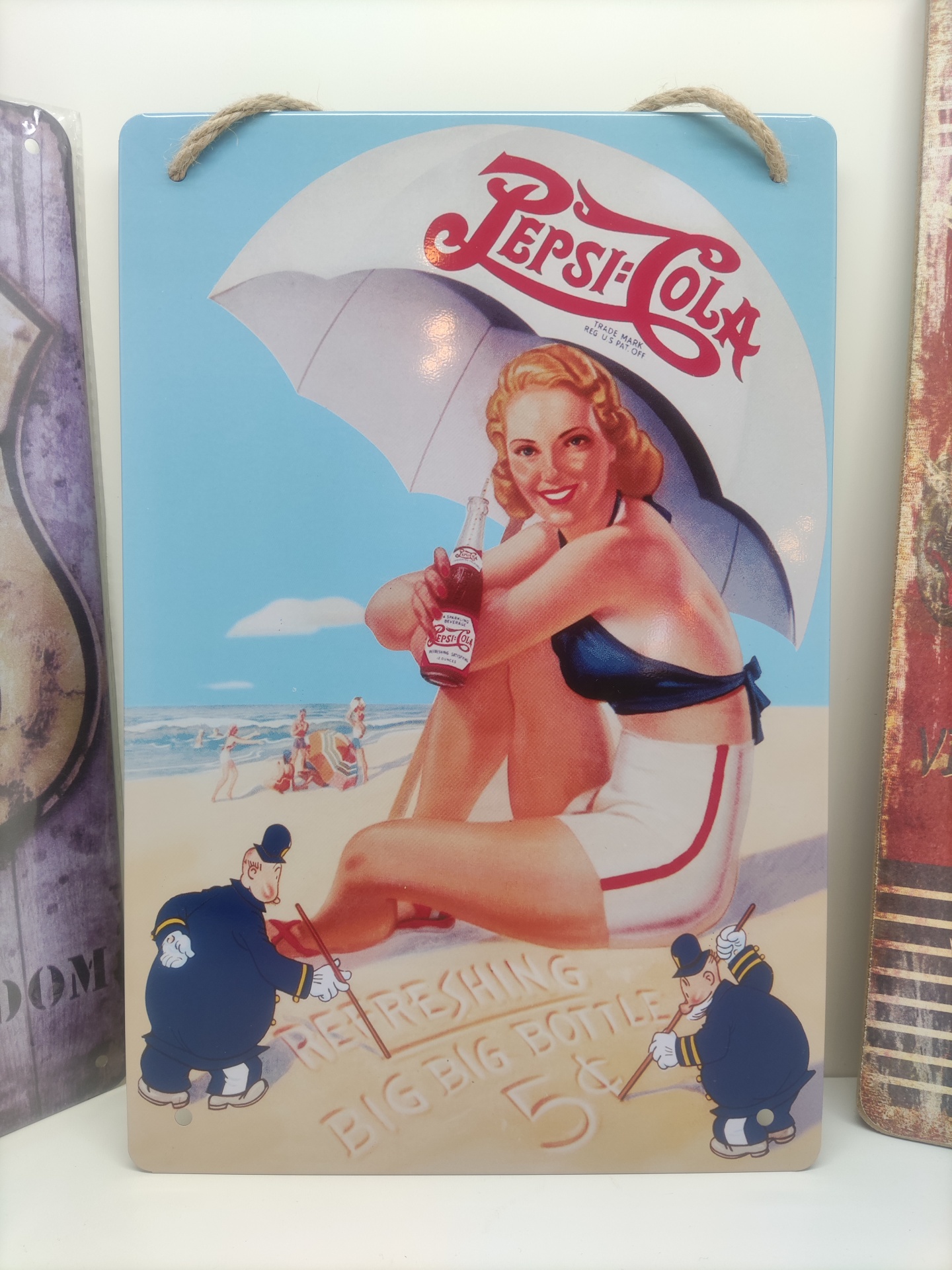 Placa metálica vintage com mulher na praia segurando garrafa de Pepsi-Cola sob guarda-sol