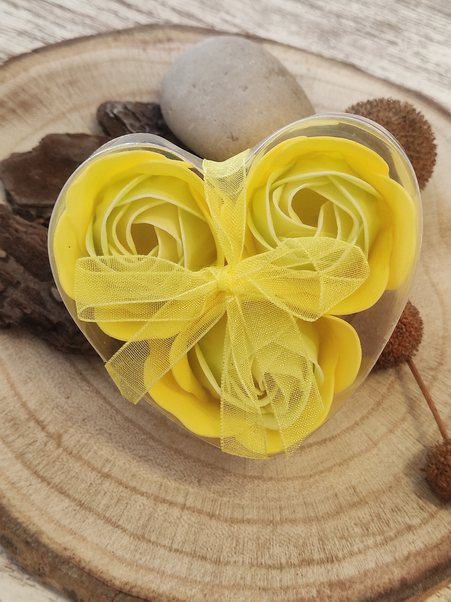 Caixa em forma de coração com flores amarelas artificiais e fita amarela sobre base de madeira redonda