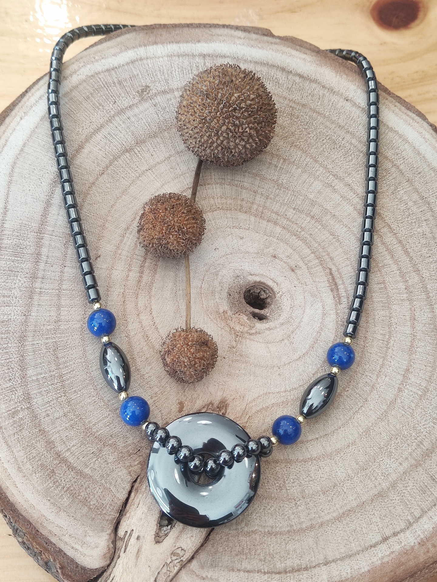 Colar com contas metálicas prata e azuis e peça central redonda sobre madeira