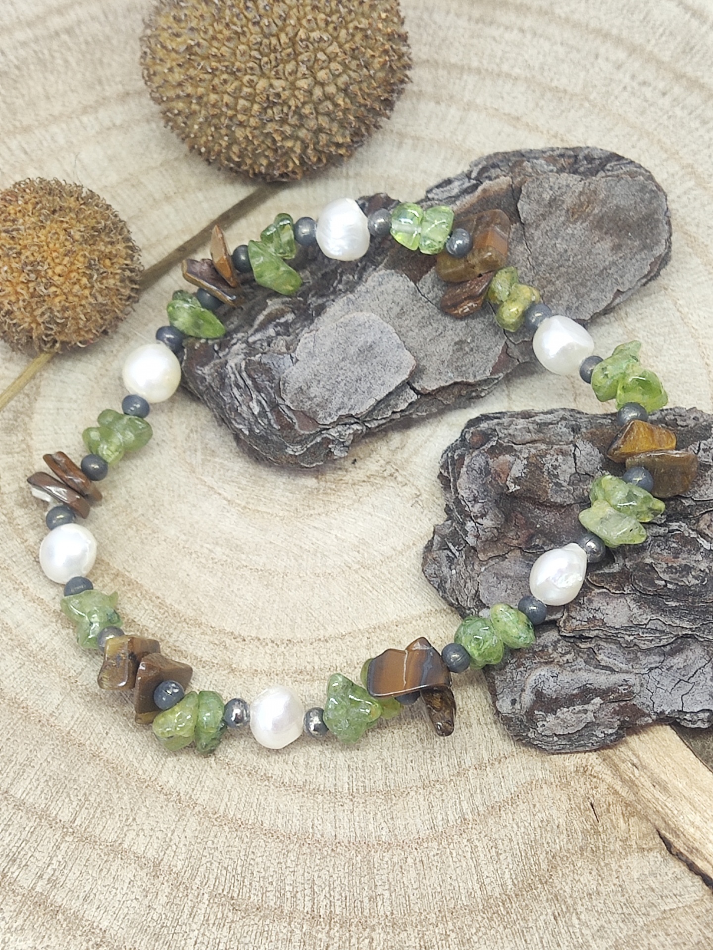 Pulseira artesanal com pedras verdes, olho de tigre, pérolas e contas pretas sobre madeira