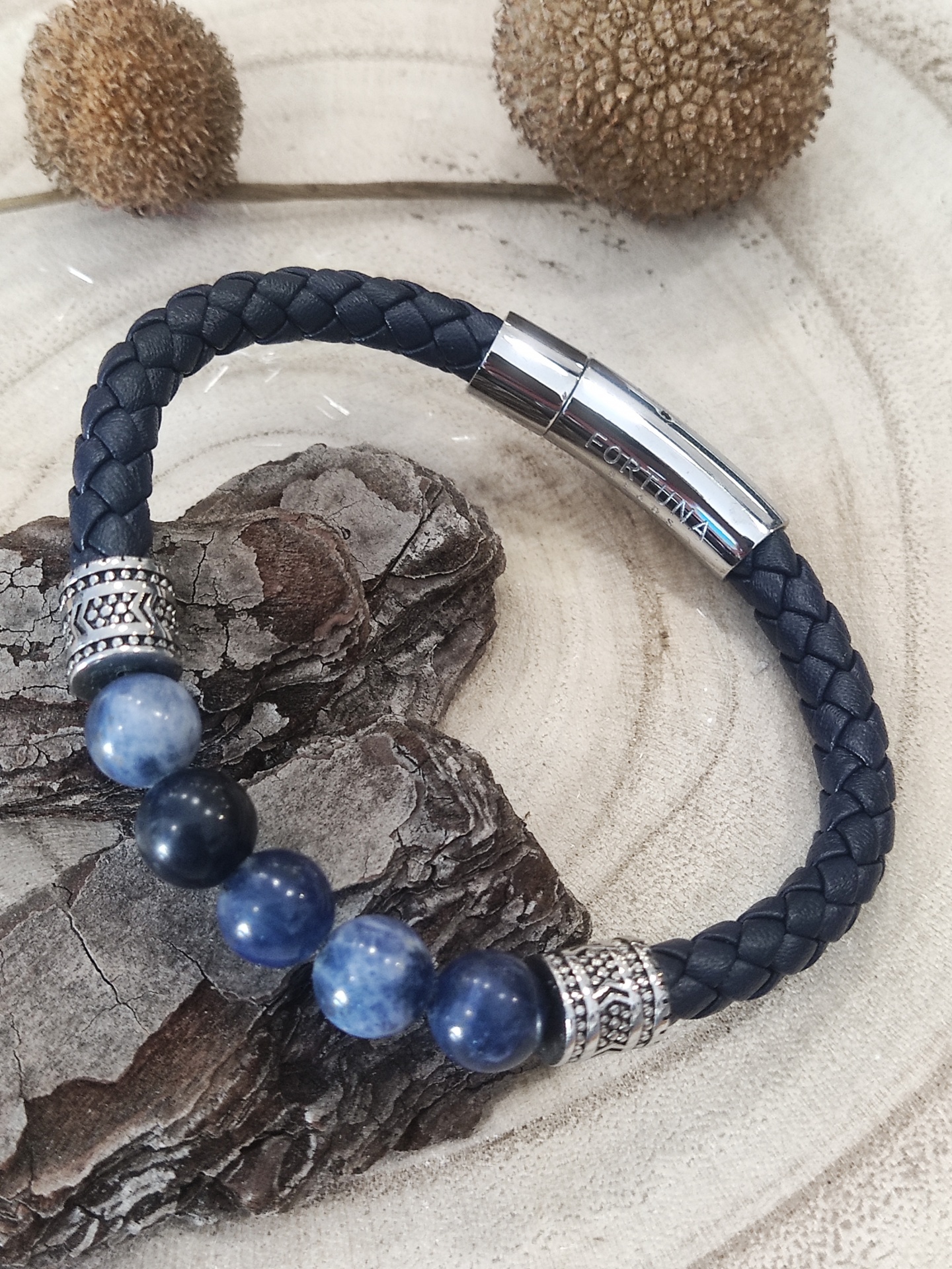 Pulseira preta com contas azuis e fecho prateado gravado PORTIMÃO sobre superfície de madeira