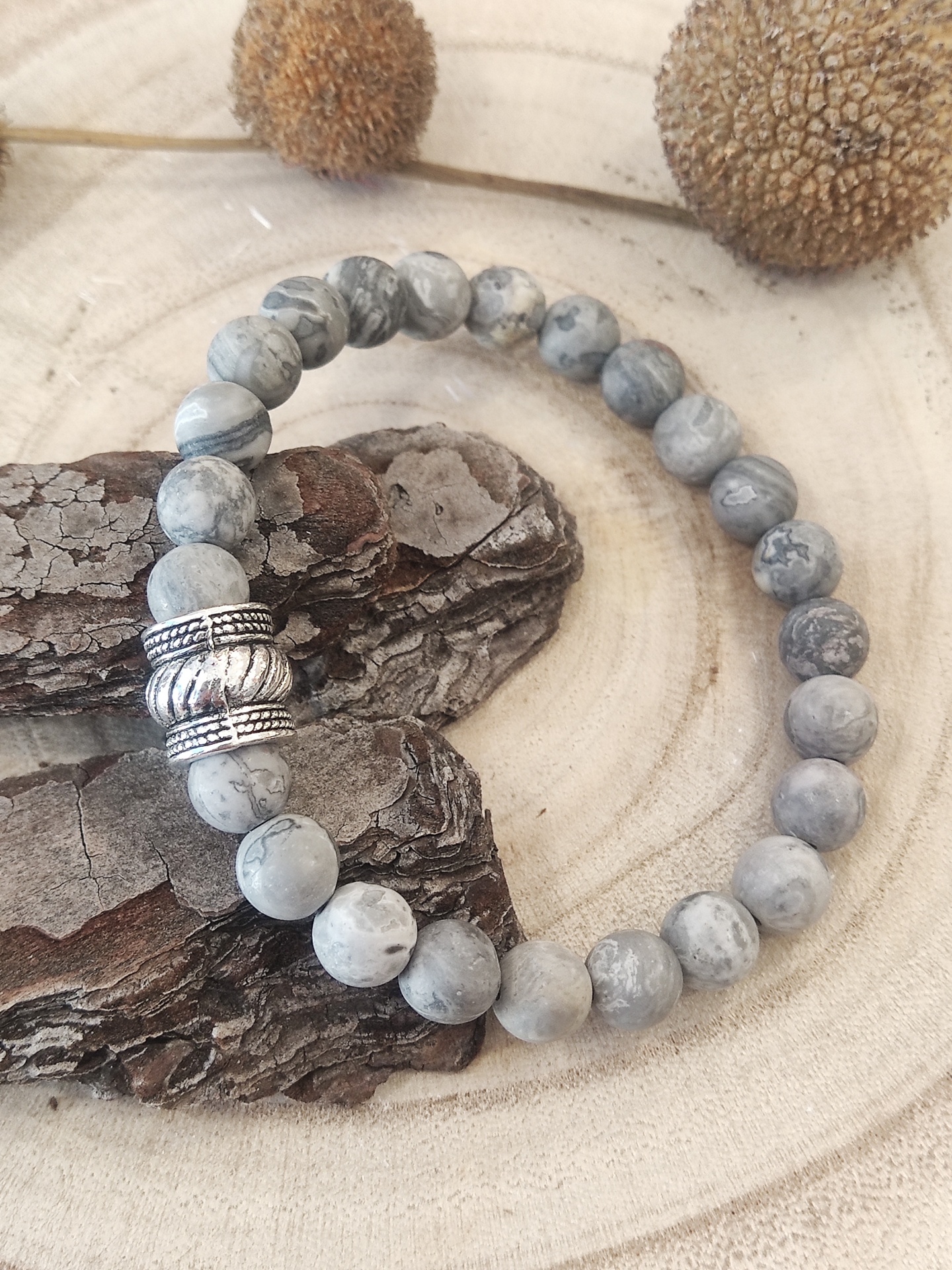 Pulseira de contas cinza marmorizadas com detalhes prateados sobre madeira