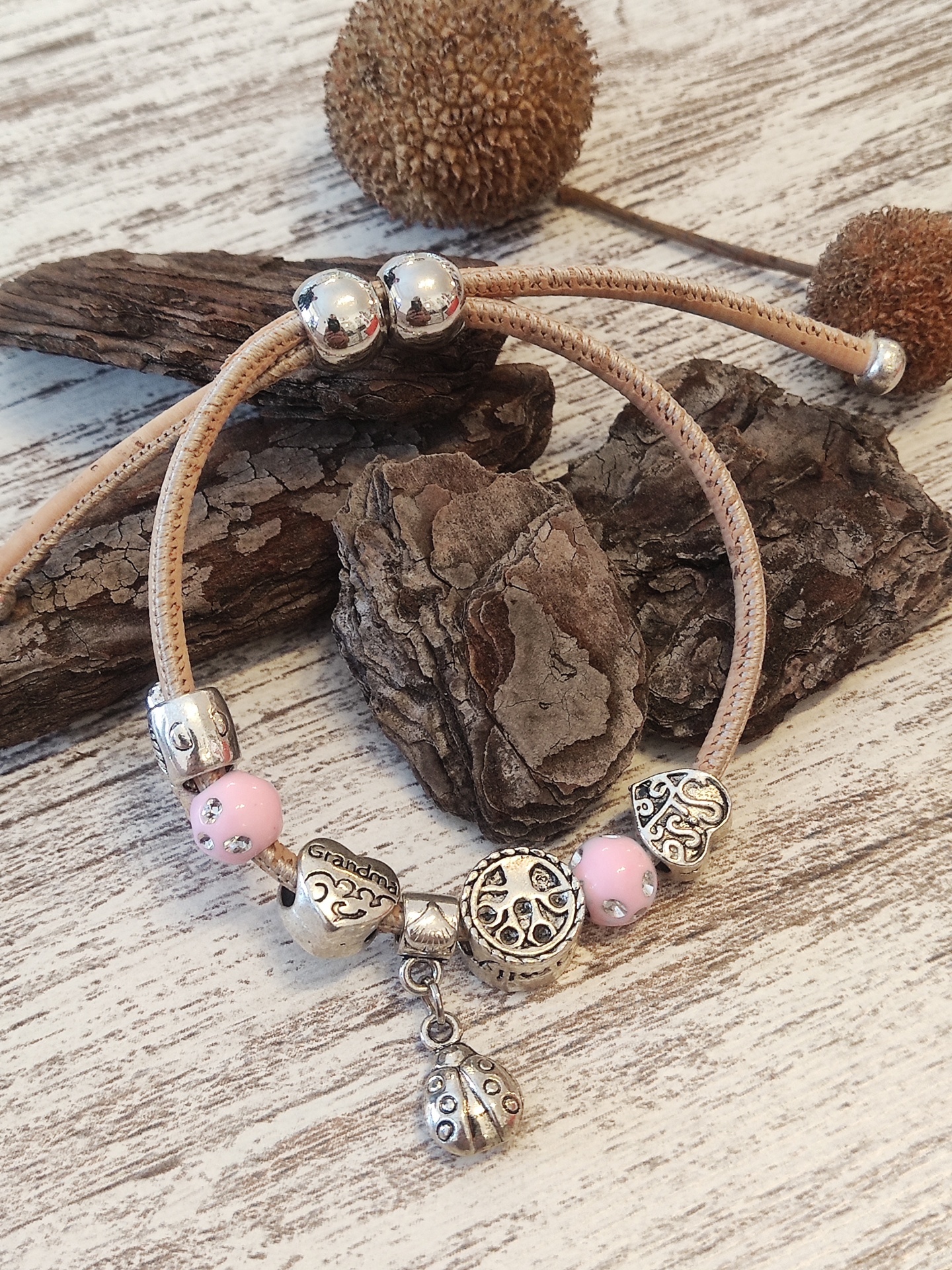 Pulseira ajustável com contas metálicas e rosas sobre madeira clara.