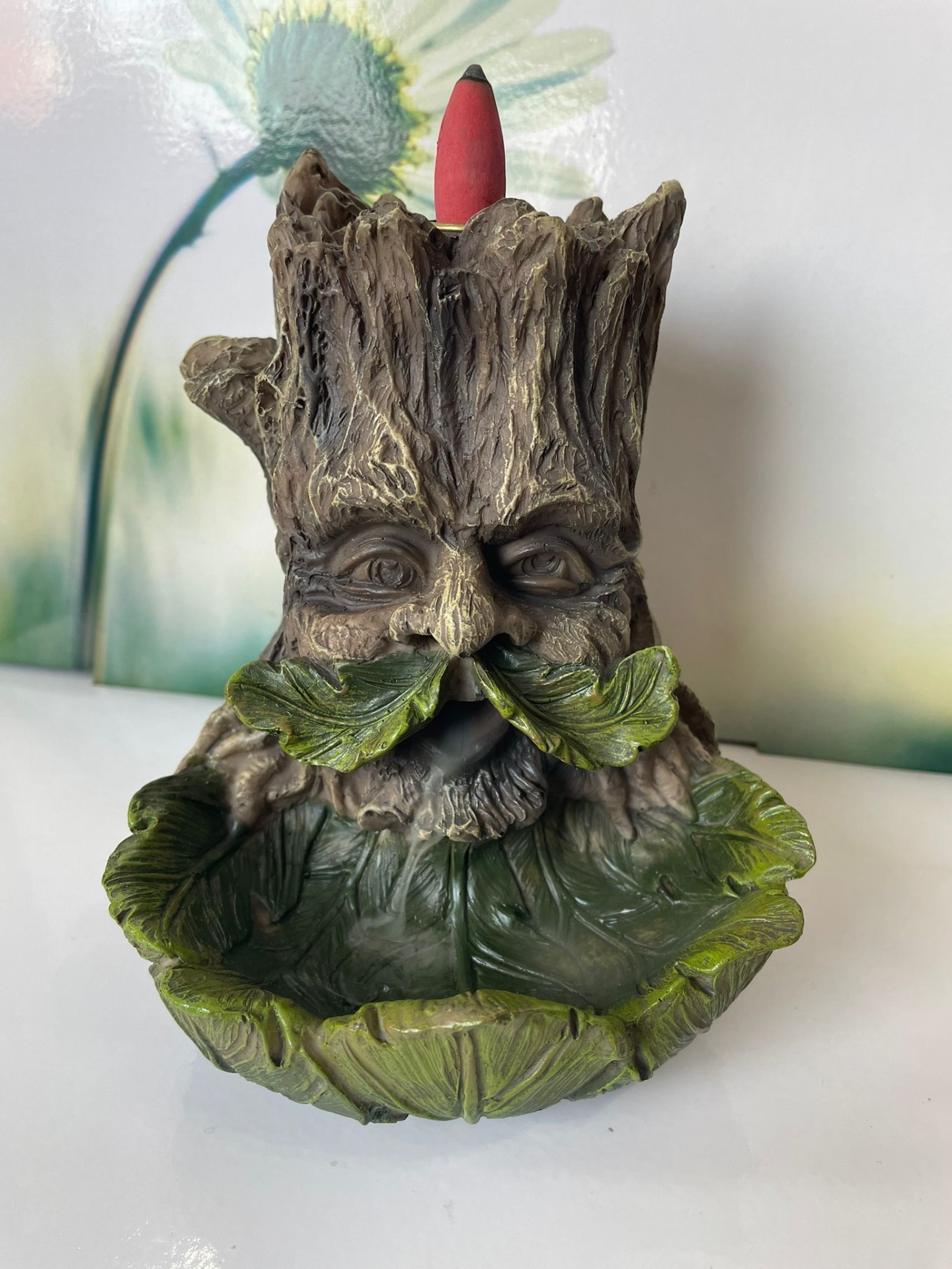 Incensário de tronco de árvore com rosto e folhas verdes, cone de incenso vermelho no topo