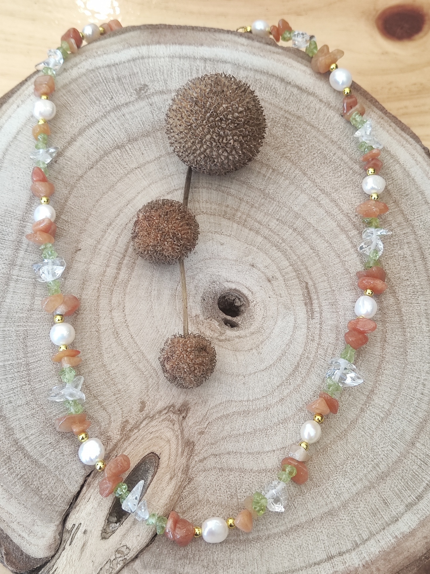 Colar colorido com pedras e pérolas sobre suporte de madeira redonda com frutos secos