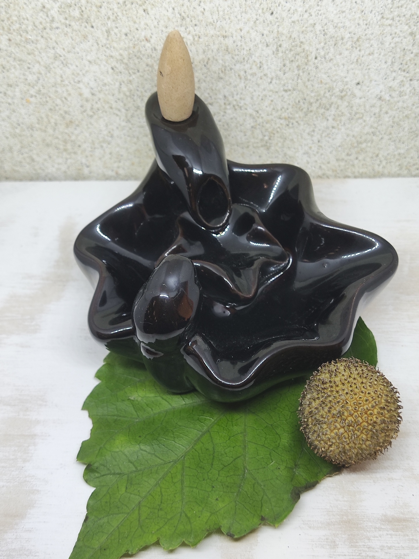 Incensário preto com cone de incenso sobre folha verde e bola marrom