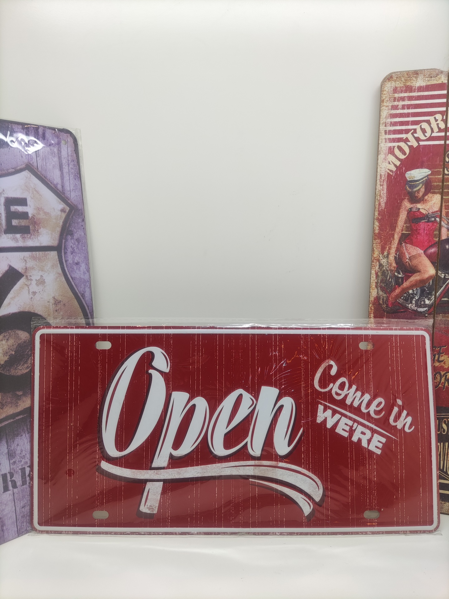 Placa vermelha decorativa com texto 'Open Come in WE'RE' em branco