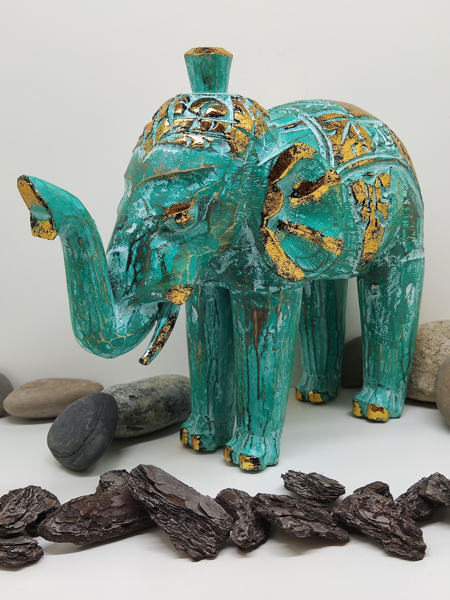 Escultura de elefante verde e dourado em madeira com pedras e cascas ao redor