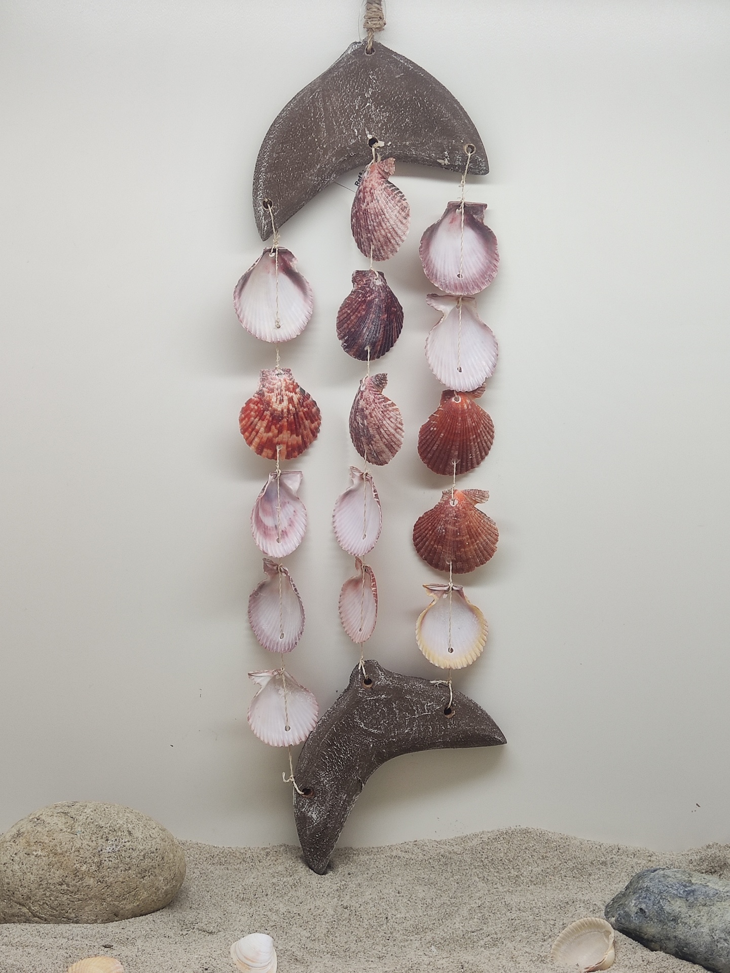 Móbile decorativo de conchas naturais pendurado com peças de madeira e areia ao fundo