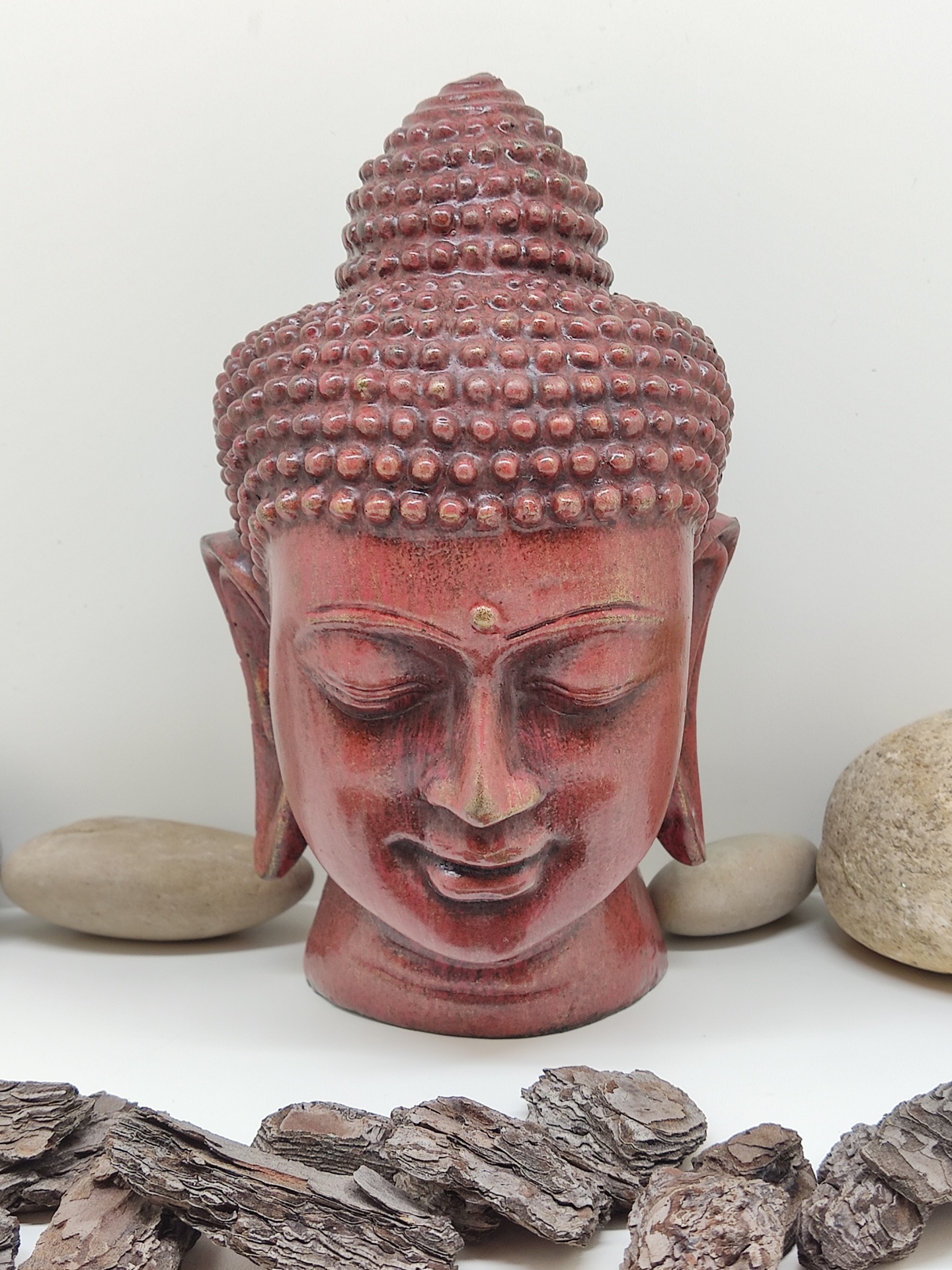 Estátua da cabeça de Buda vermelha com textura em relevo e pedras decorativas ao redor