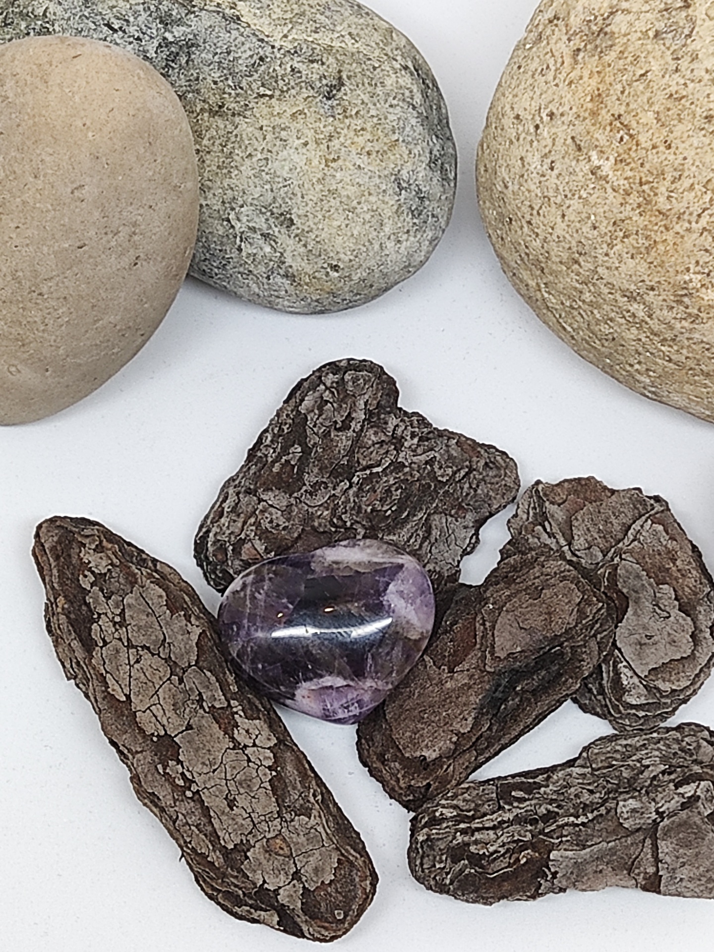 Pedra polida roxa sobre cascas de árvore e pedras maiores arredondadas