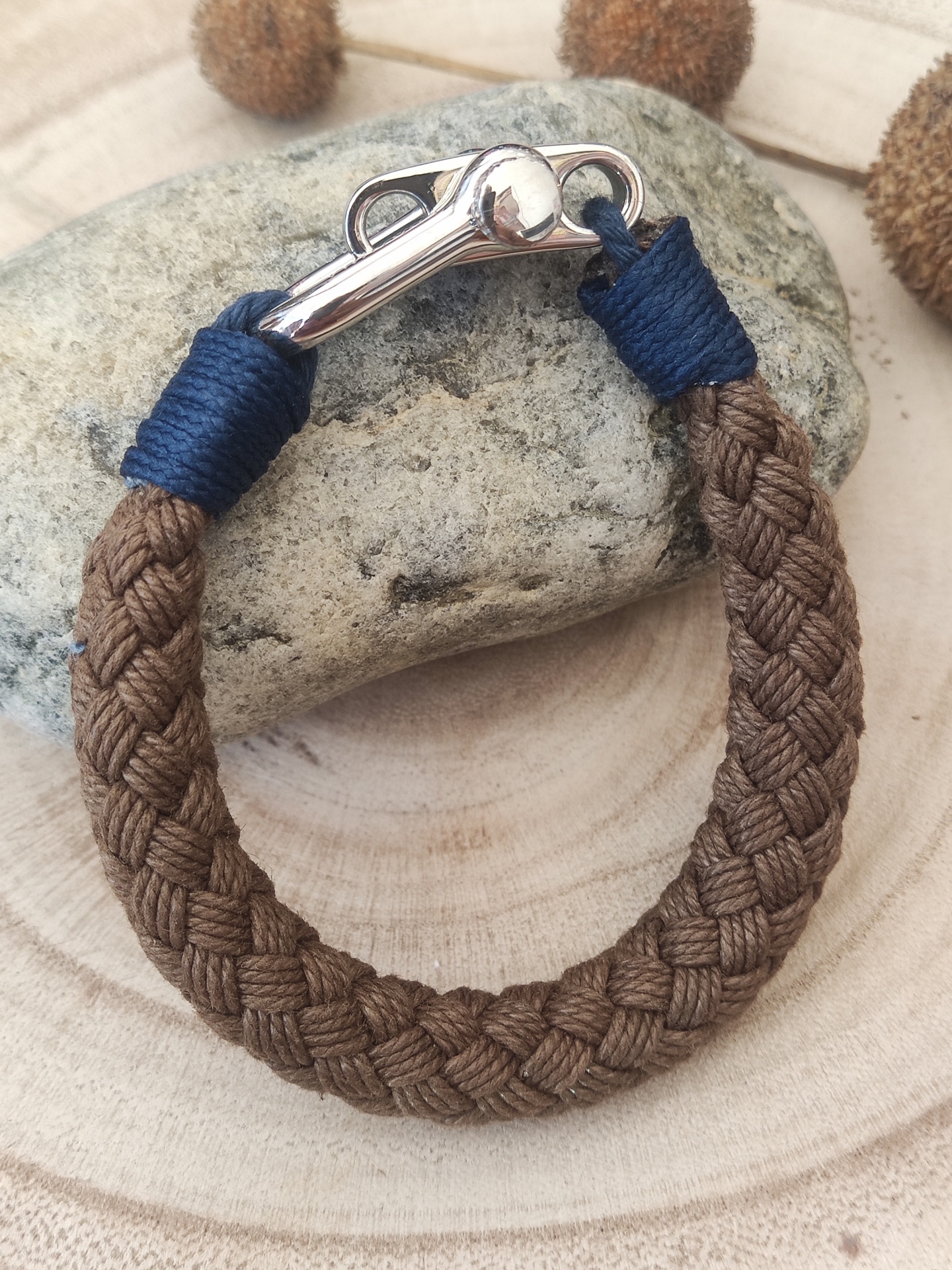 Pulseira de corda marrom trançada com fecho metálico e detalhes em azul escuro sobre pedra