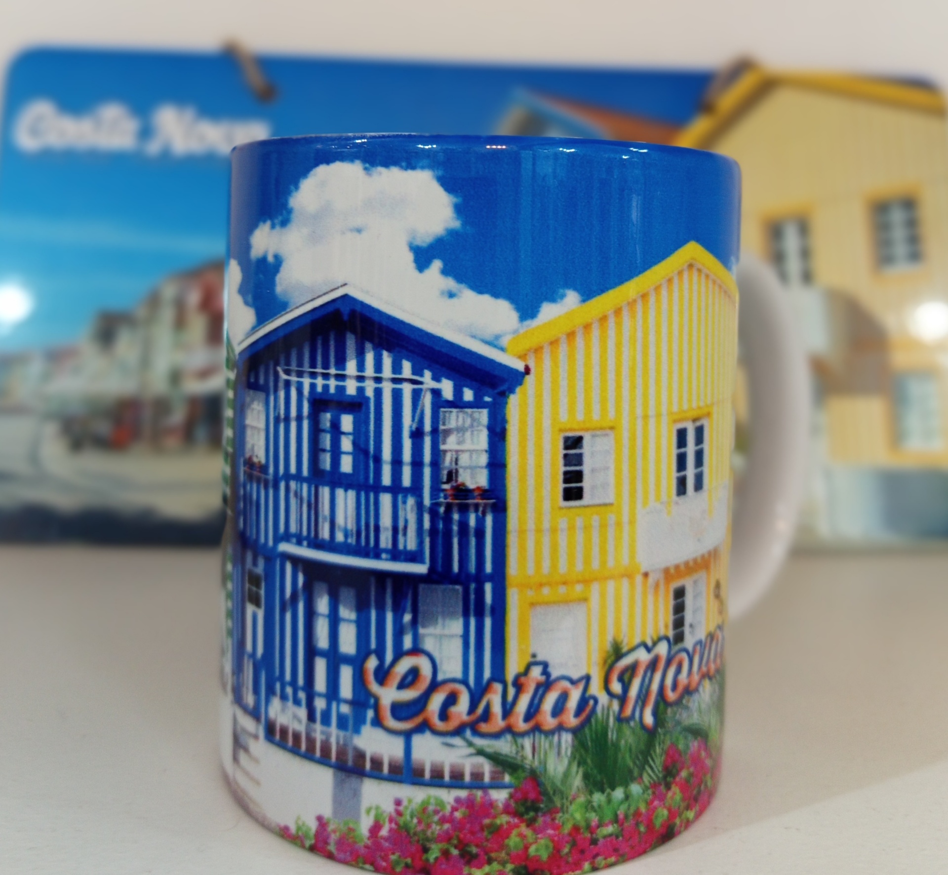 Caneca com imagem colorida de casas às riscas e texto Costa Nova