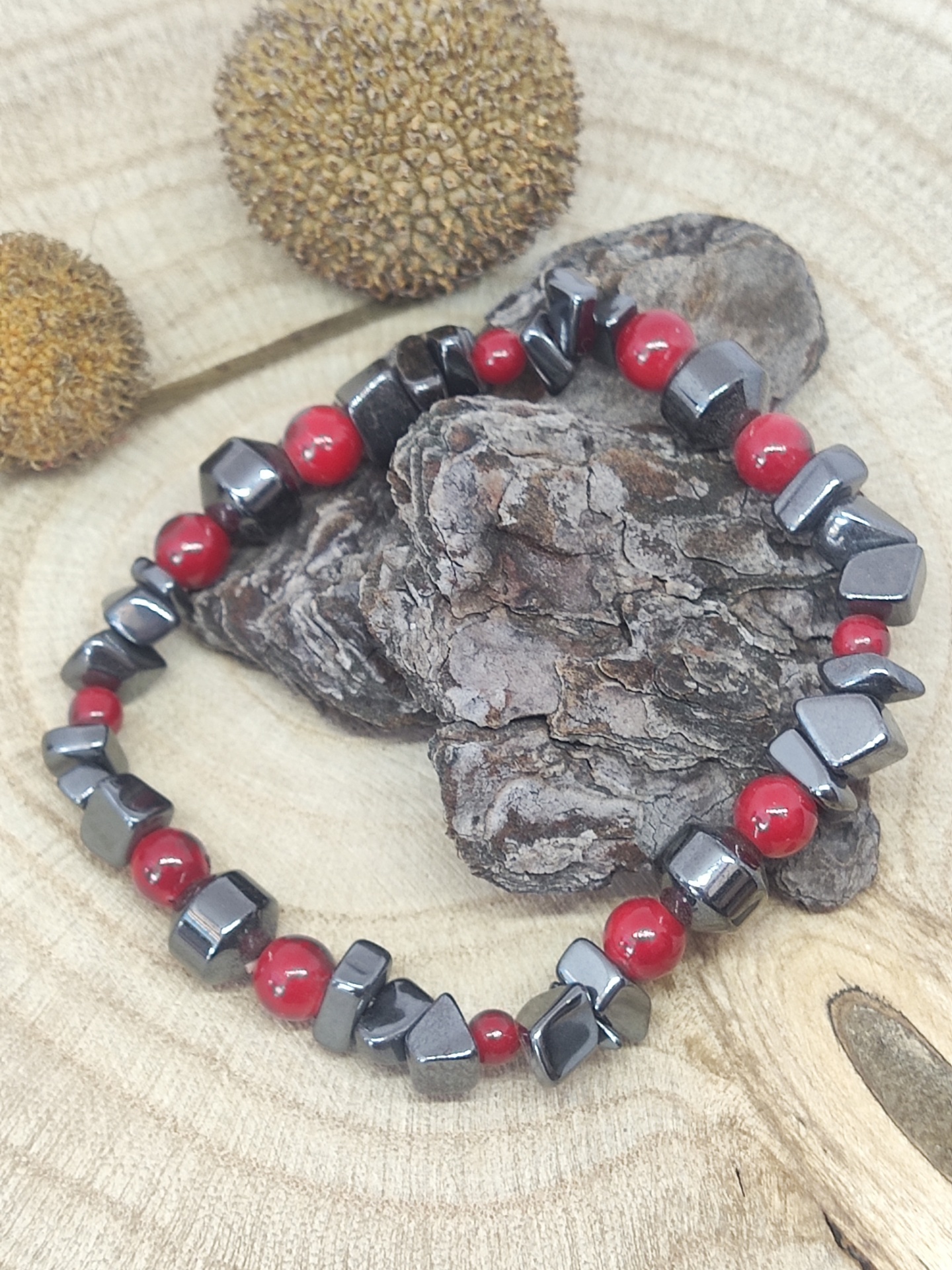 Pulseira com contas vermelhas e cinza metálico sobre fundo de madeira