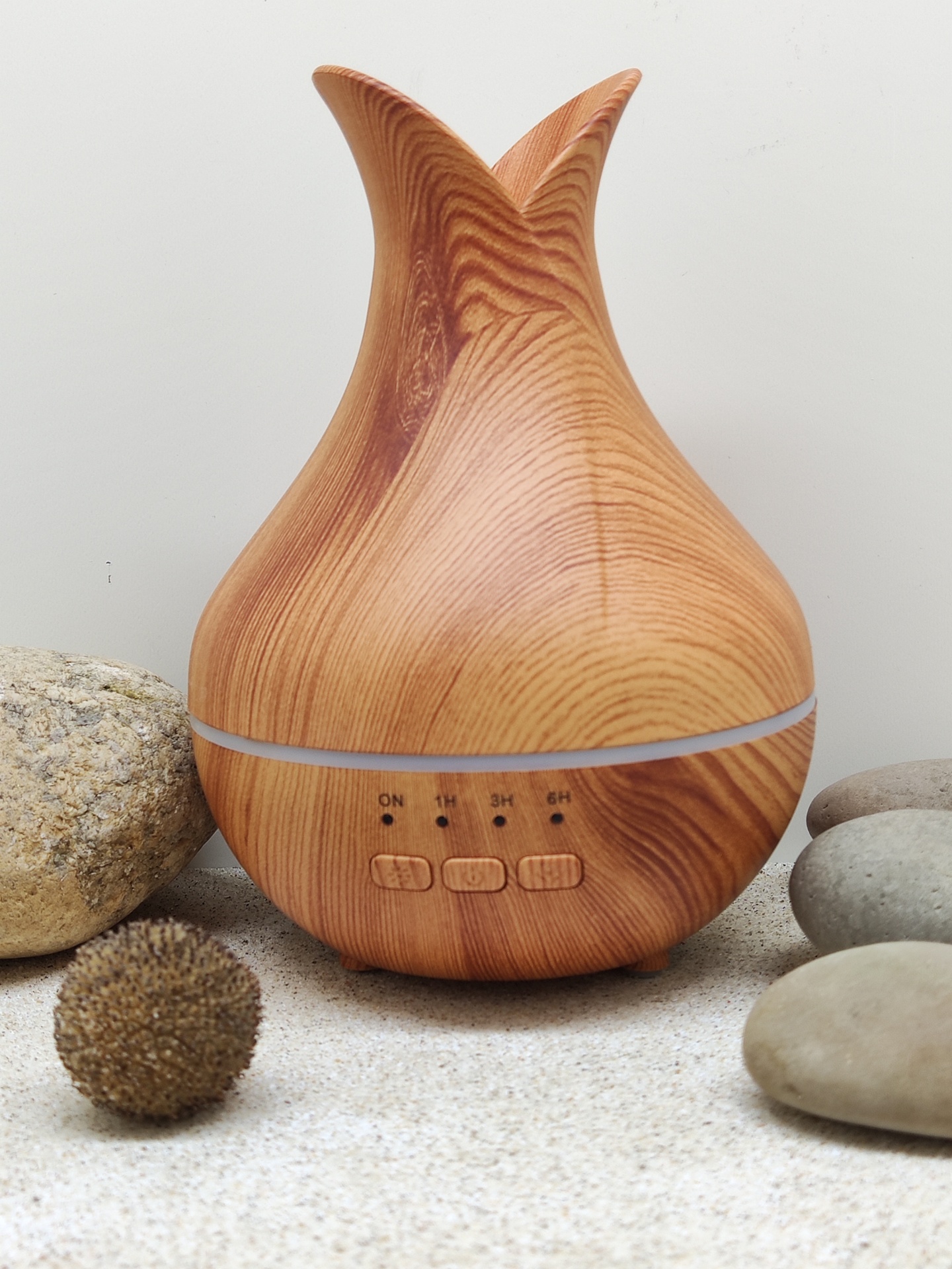 Difusor de aroma em madeira clara com botões e indicações de tempo, rodeado por pedras.