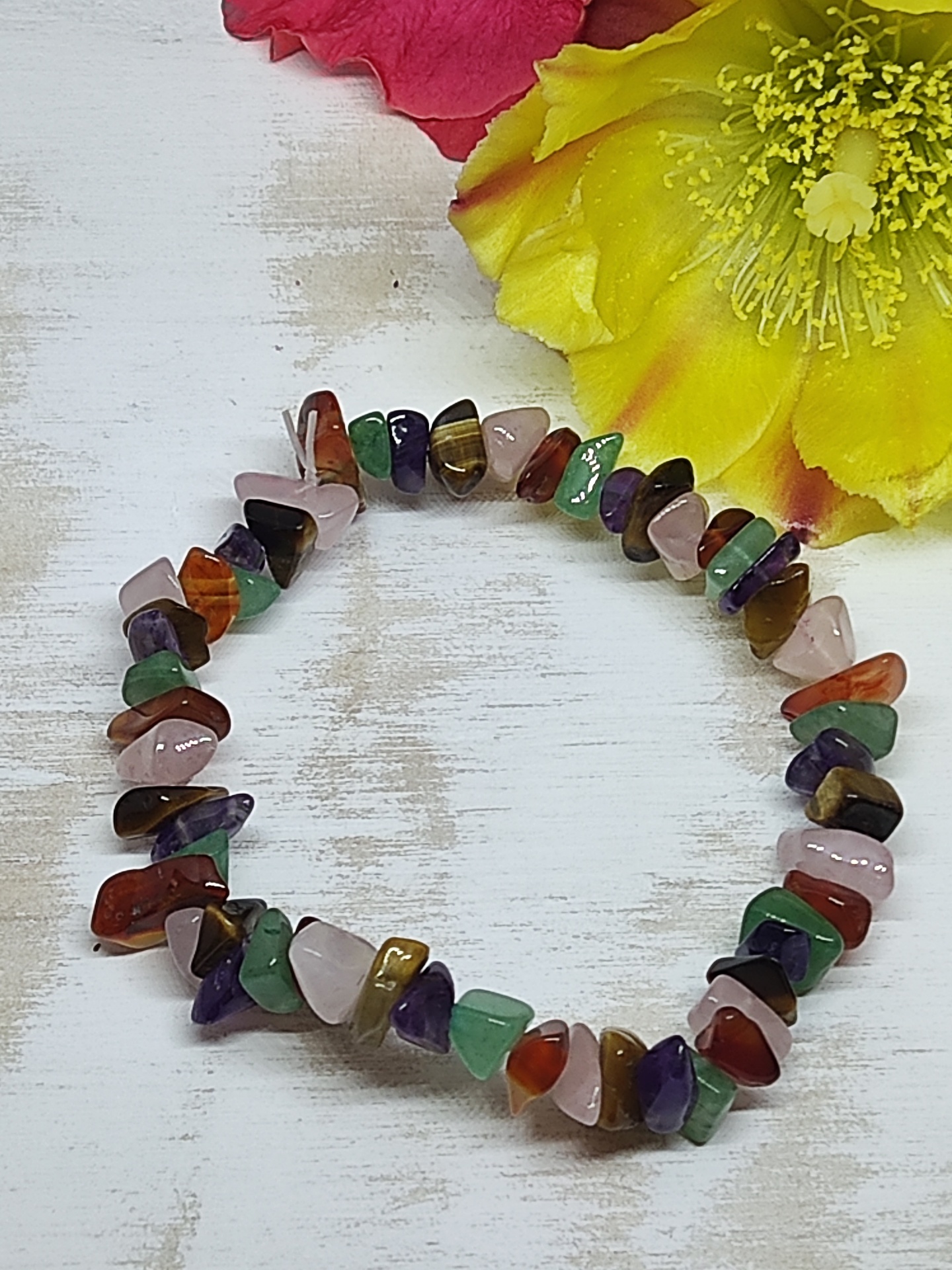 Pulseira de pedras naturais coloridas em círculo sobre superfície branca com flores