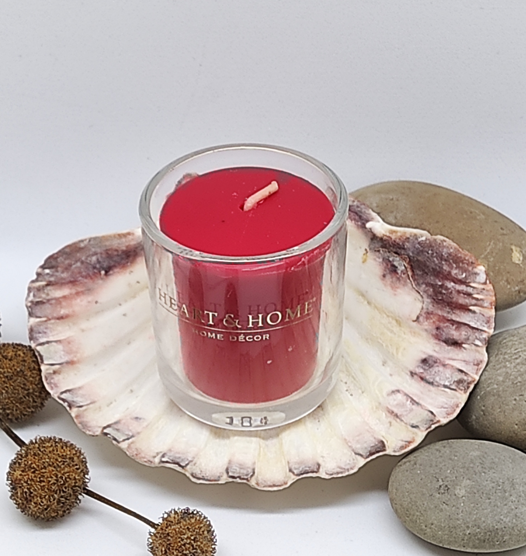 Vela vermelha em recipiente de vidro sobre concha com pedras e ramos secos