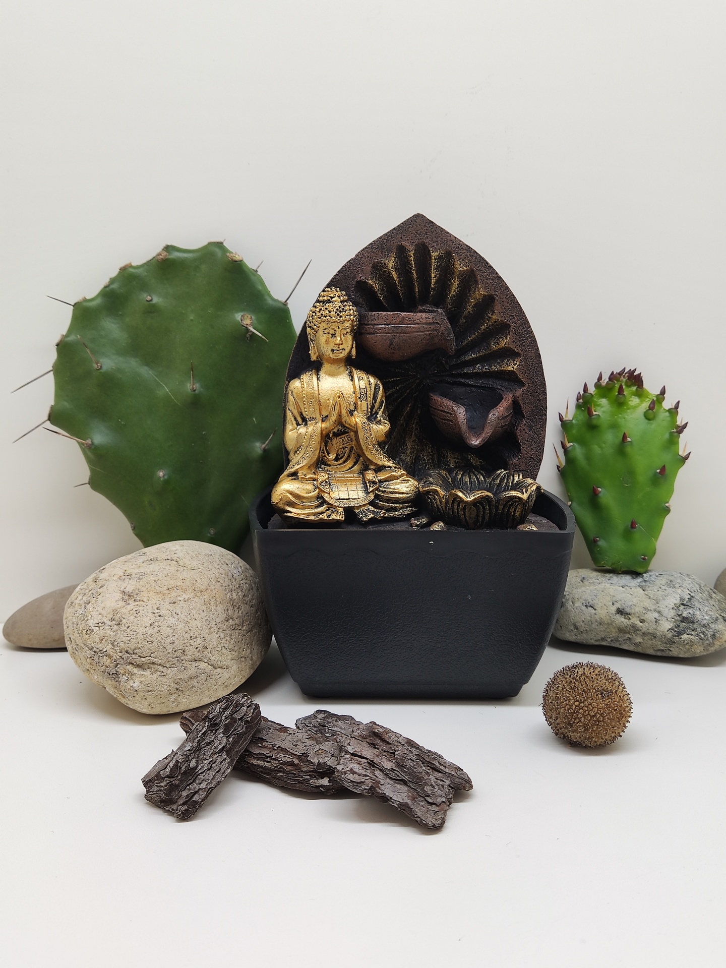 Fonte decorativa preta com estátua dourada de Buda entre pedras e cactos
