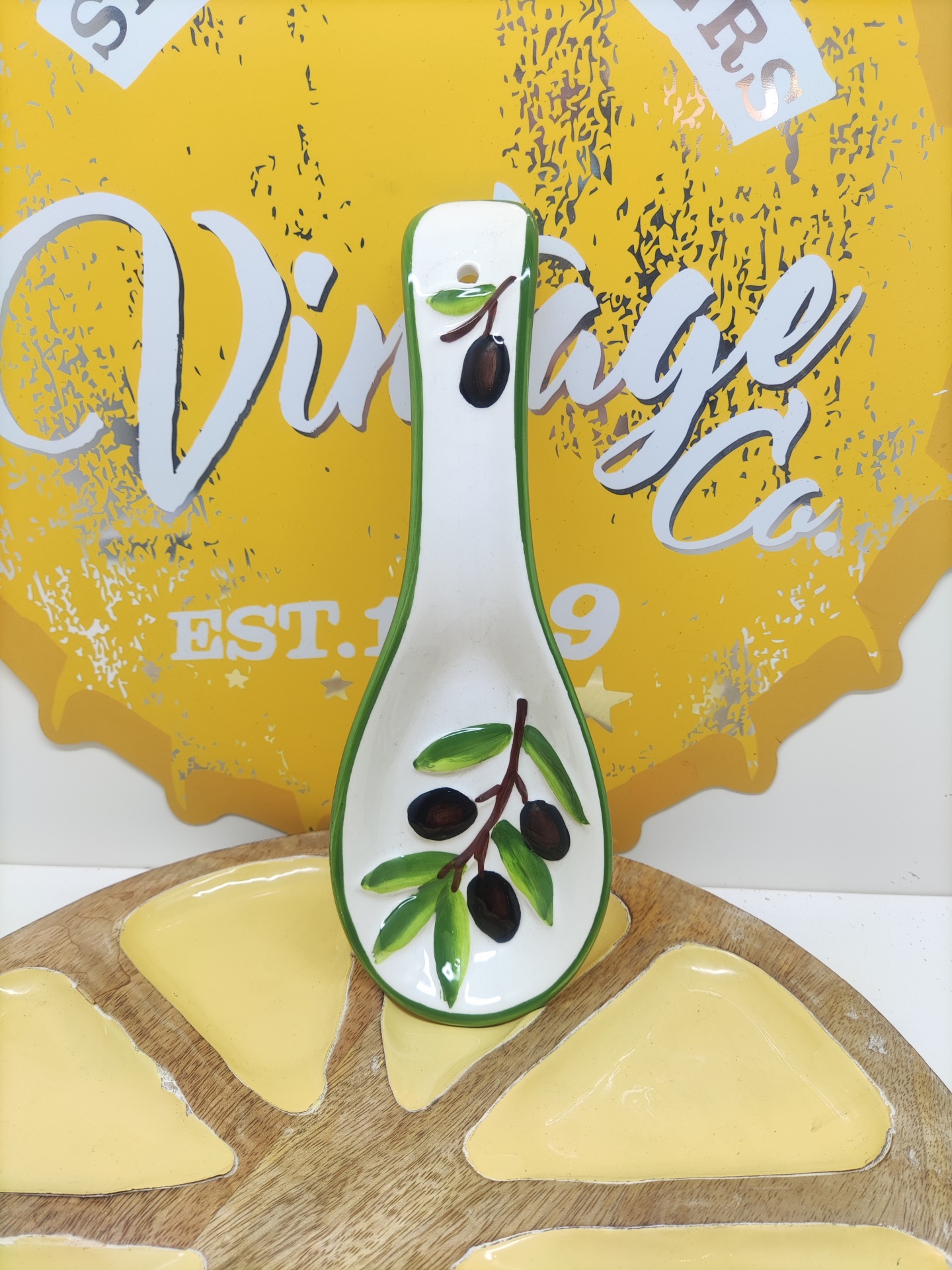 Colher de cerâmica branca decorada com azeitonas em fundo amarelo