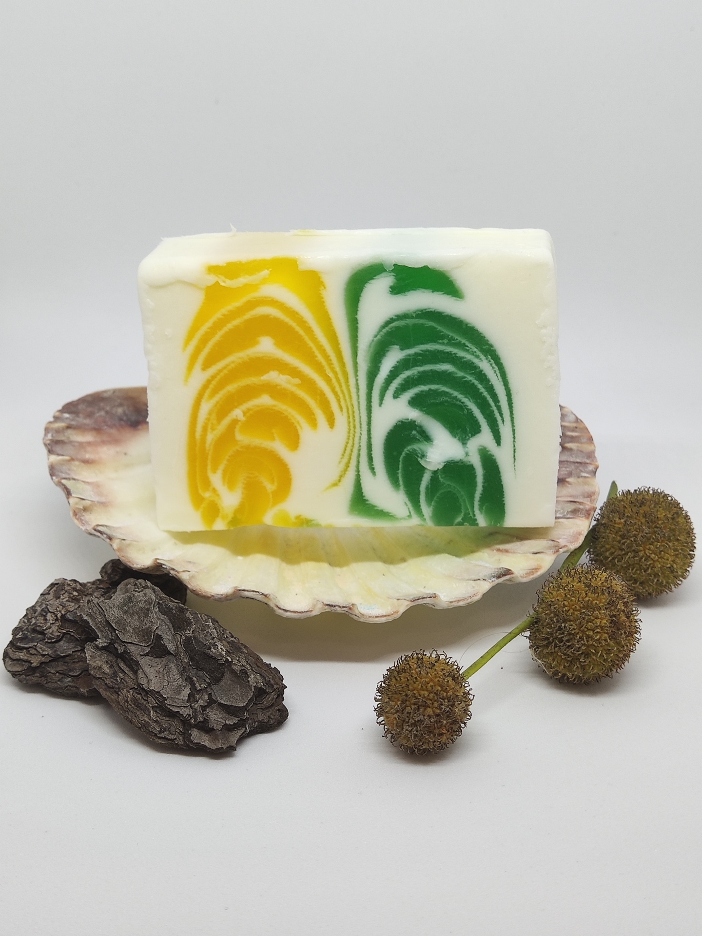 Sabonete artesanal com padrões amarelo e verde sobre concha com natureza morta