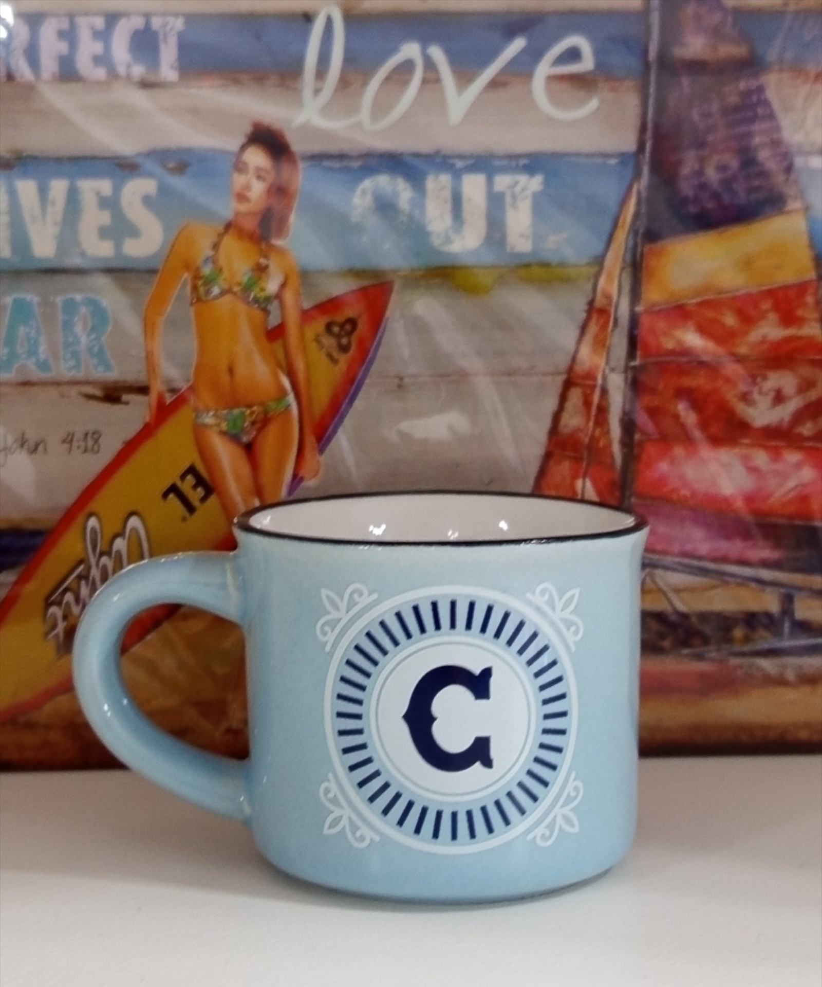 Caneca azul claro com letra C em círculo, com fundo de imagem de mulher de biquíni e prancha de surf