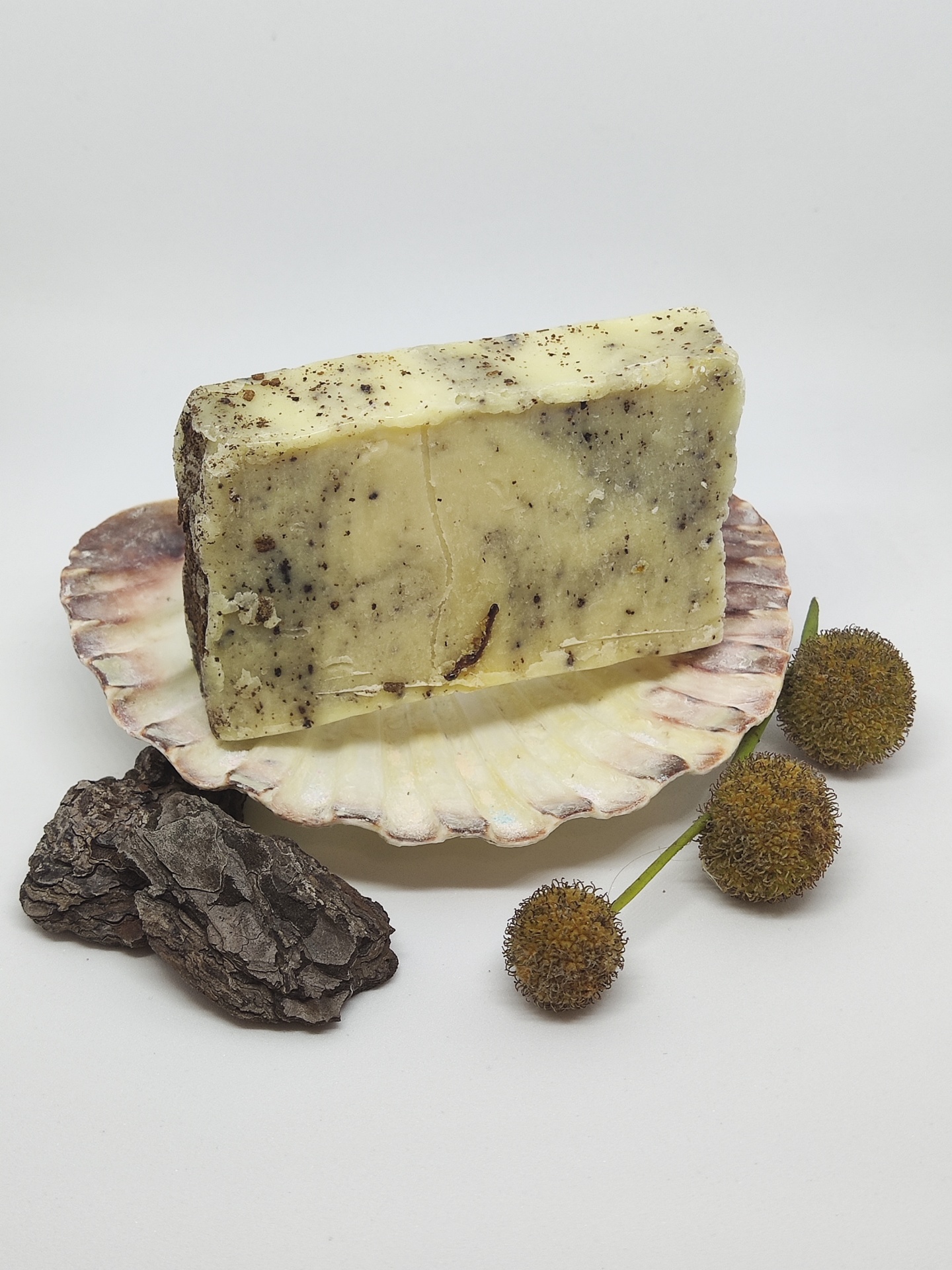 Sabonete marmoreado amarelo e castanho sobre concha, com sementes e casca de árvore