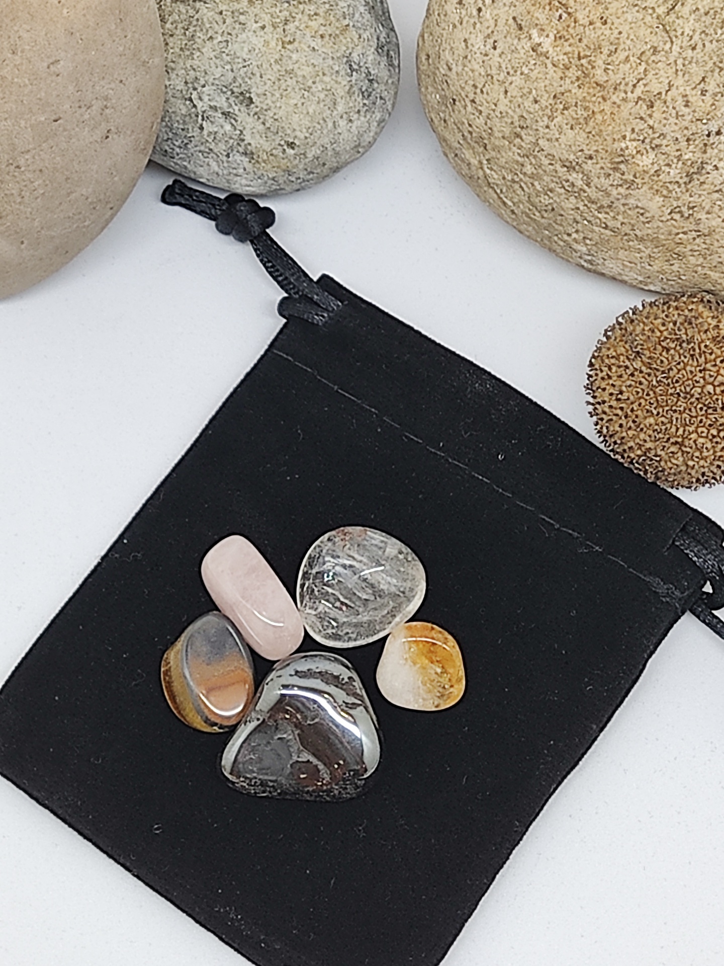 Cinco pedras polidas coloridas sobre saco preto com pedras maiores ao fundo