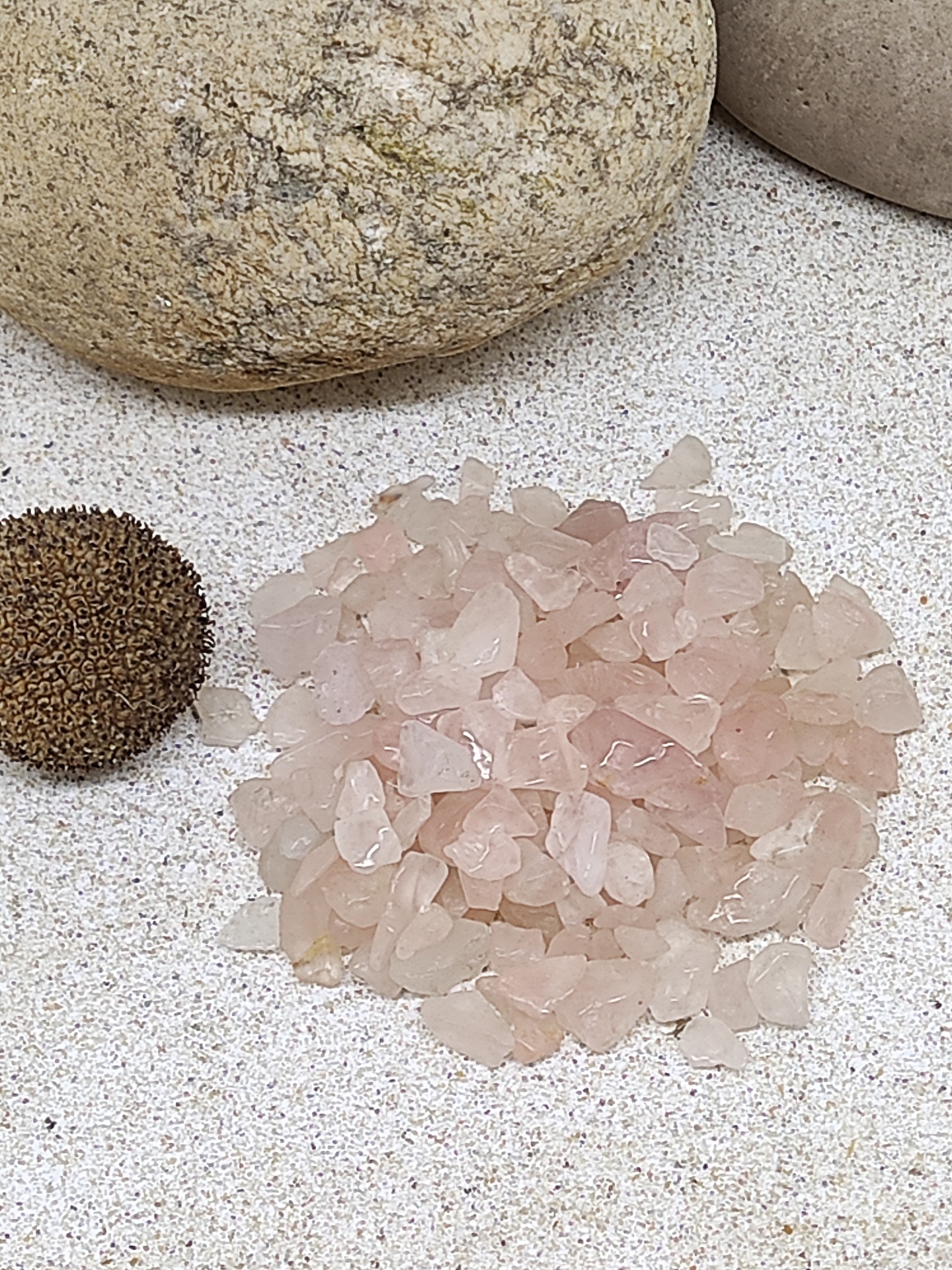 Montão de cristais rosa translúcidos ao lado de esfera marrom texturizada e pedras arredondadas