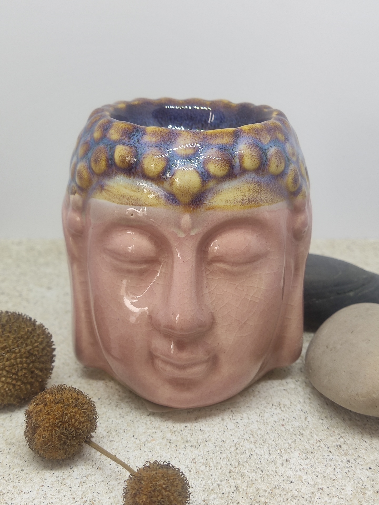 Vaso cerâmico em forma de cabeça de Buda com pedras e flores secas ao redor