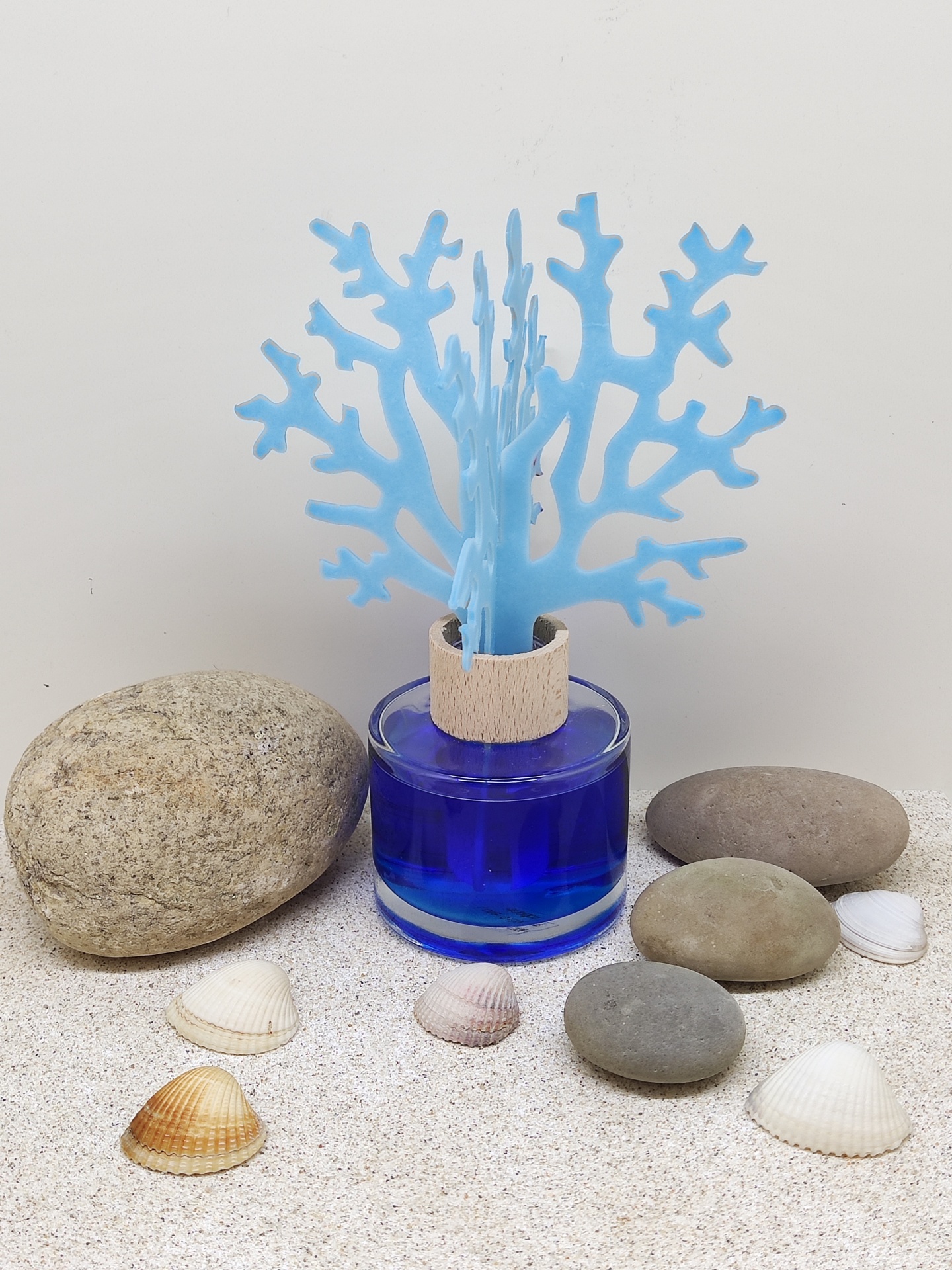 Frasco azul com paus decorativos azuis, pedras e conchas em areia