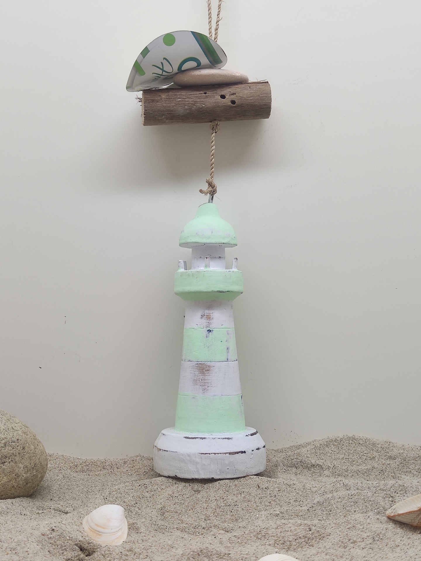 Farol decorativo de madeira verde e branco pendurado sobre areia com conchas