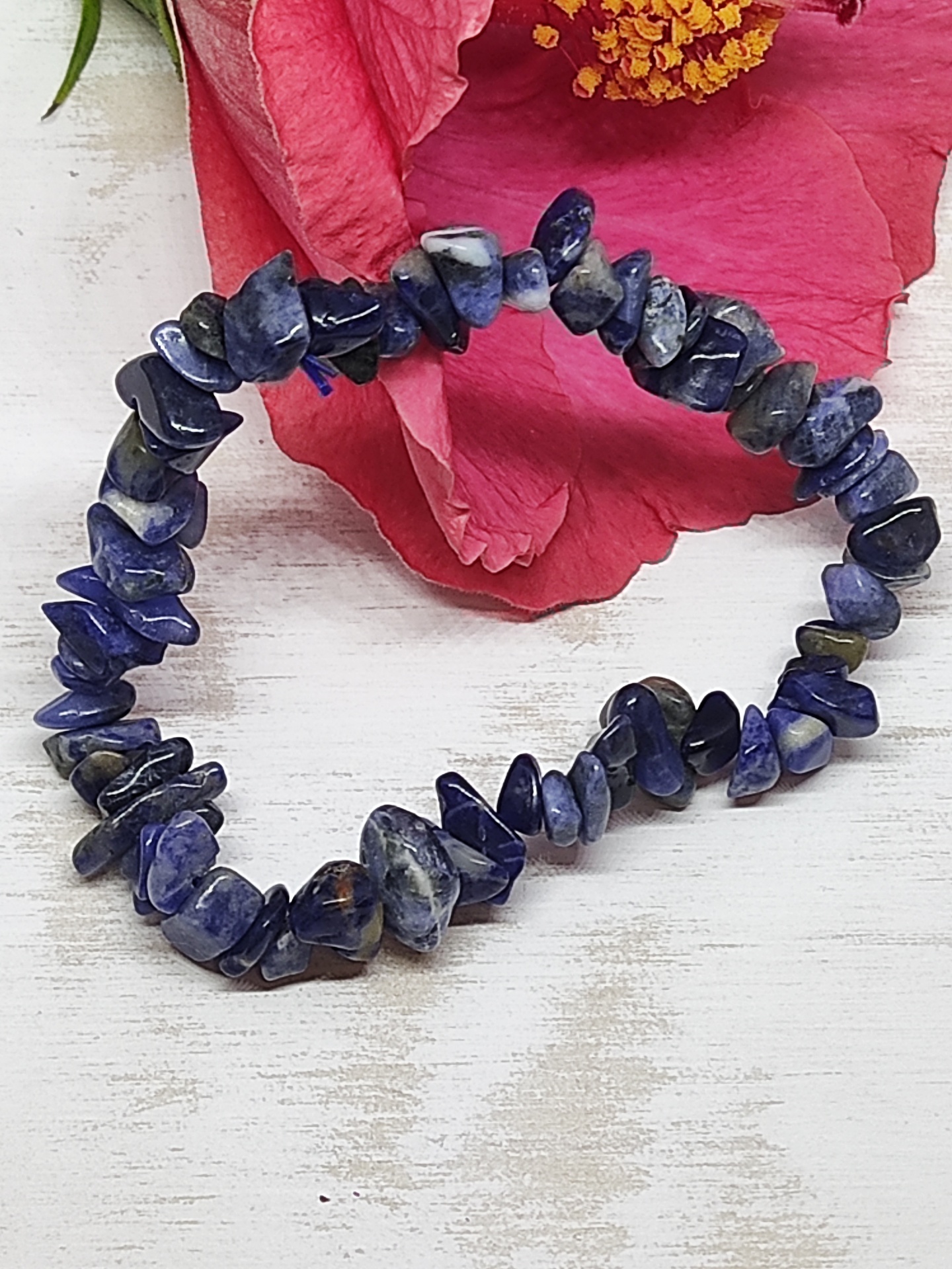 Pulseira de pedras azuis sobre superfície branca com flor rosa ao fundo