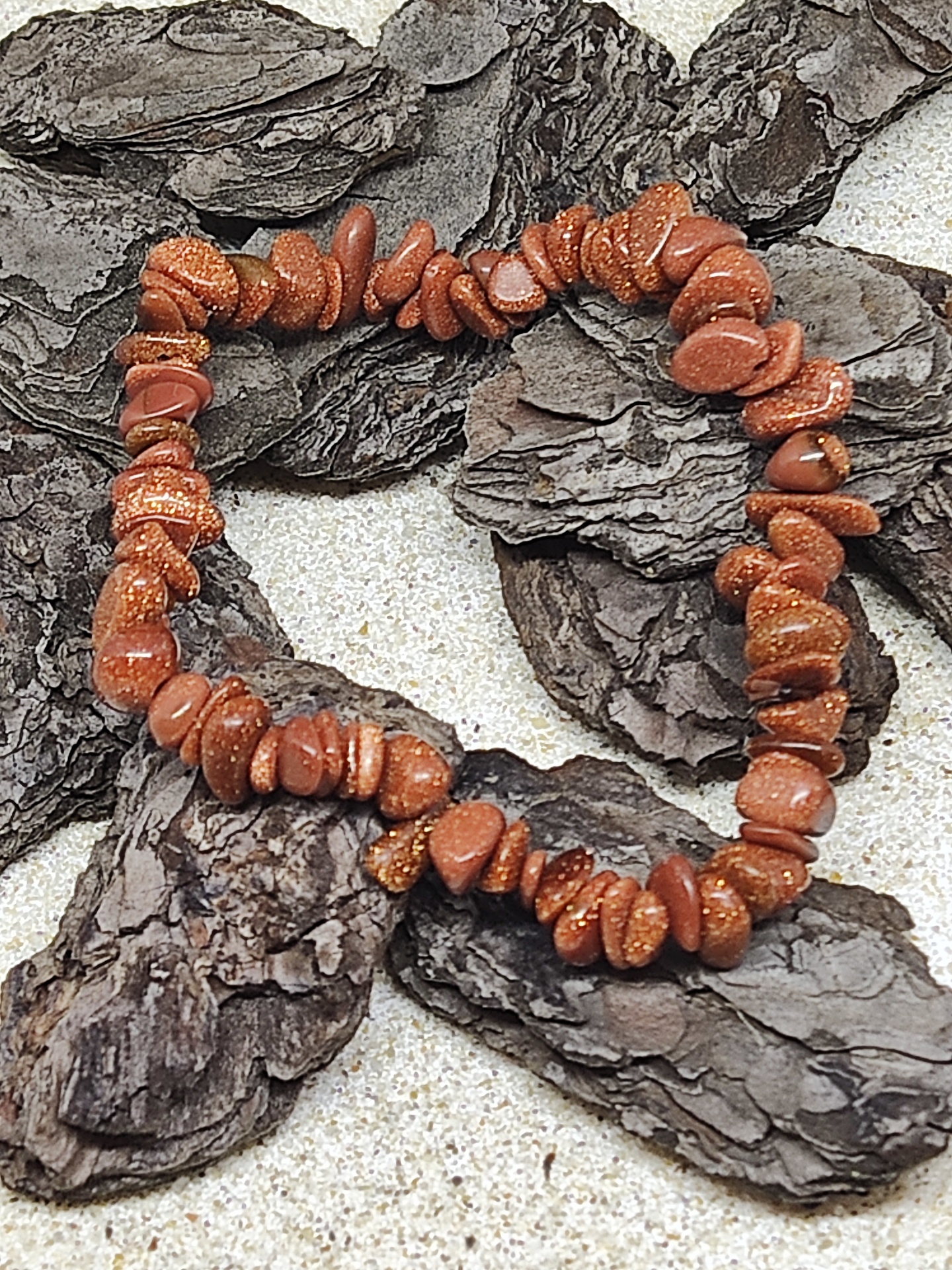 Pulseira de pedras castanho-avermelhadas com brilho dourado sobre cascas de árvore