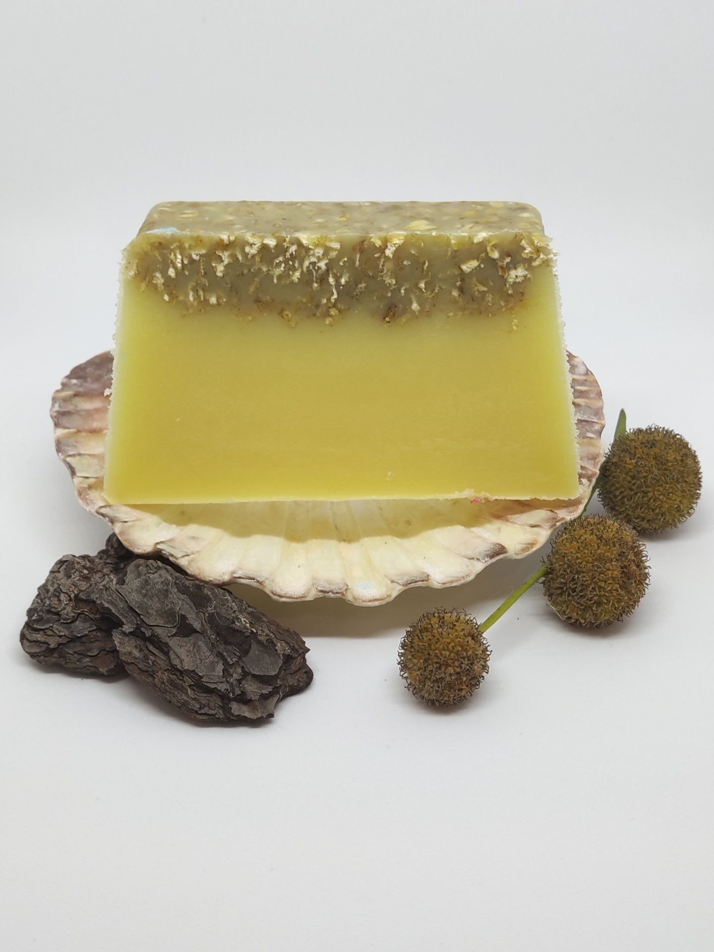 Sabão amarelo artesanal numa concha com casca e flores secas em fundo branco