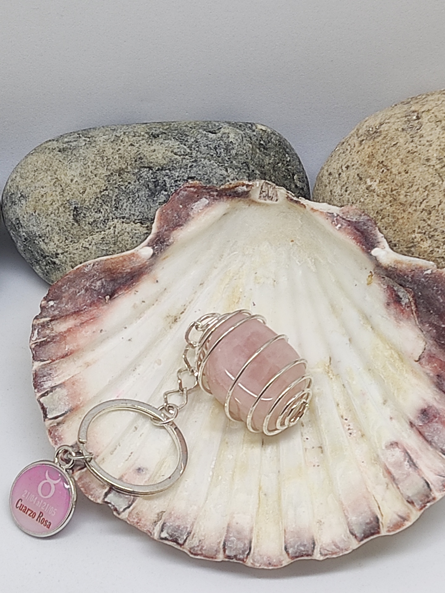 Chaveiro com pedra rosa em concha decorativa com pedras ao fundo