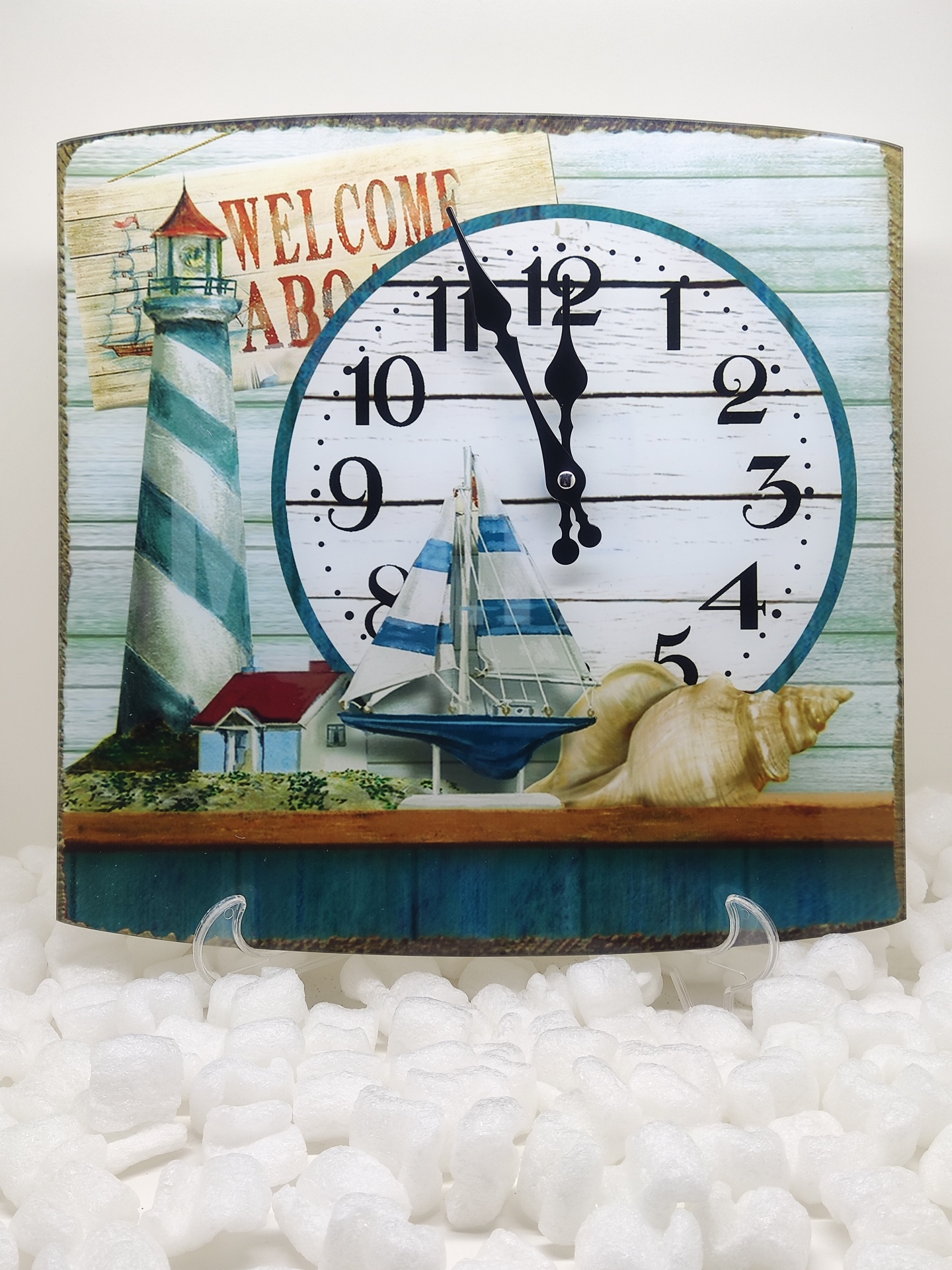 Relógio decorativo com tema náutico, incluindo farol, barco à vela, conchas e texto de boas-vindas.