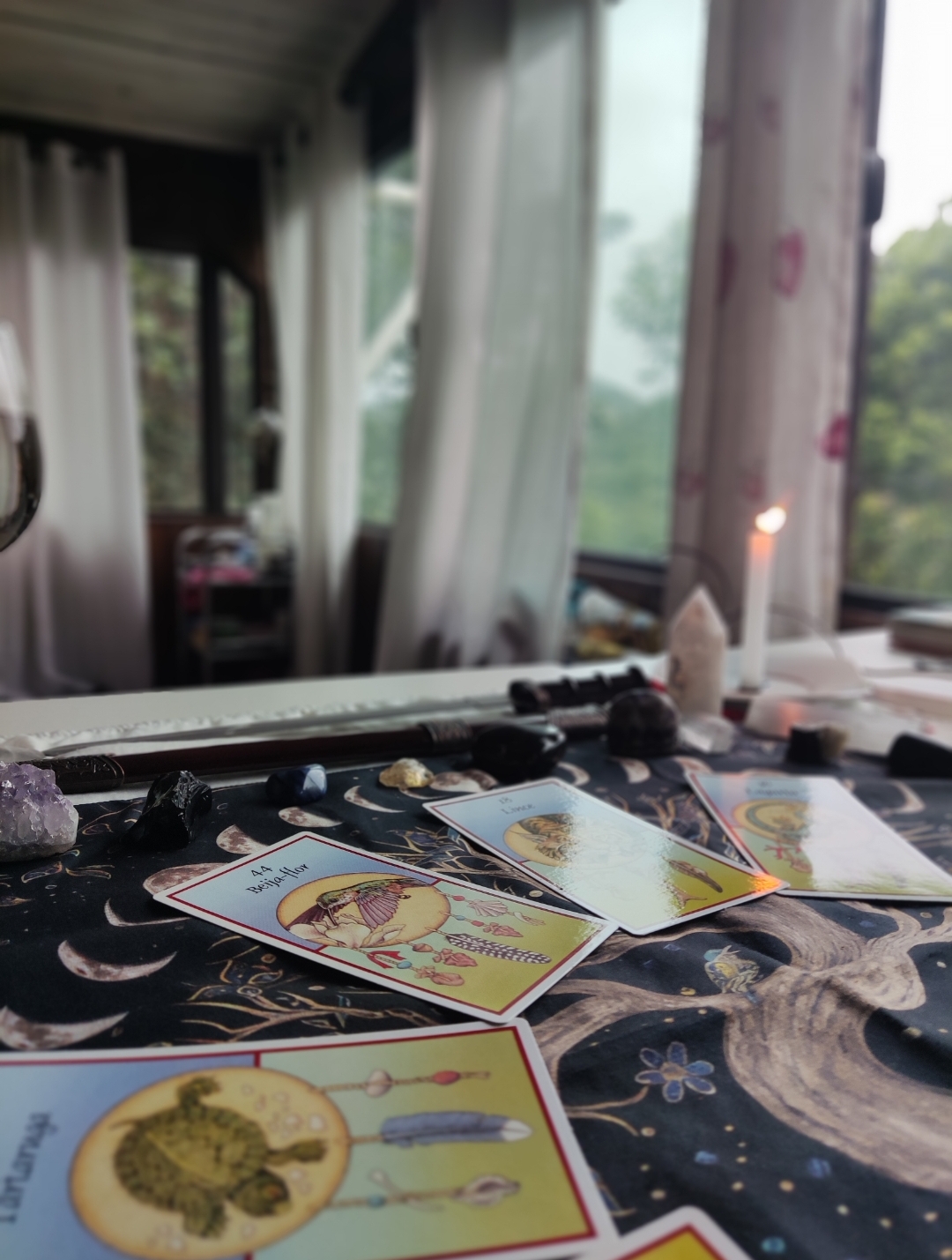 Cartas de oráculo sobre tecido com padrões lunares e pedras com vela ao fundo