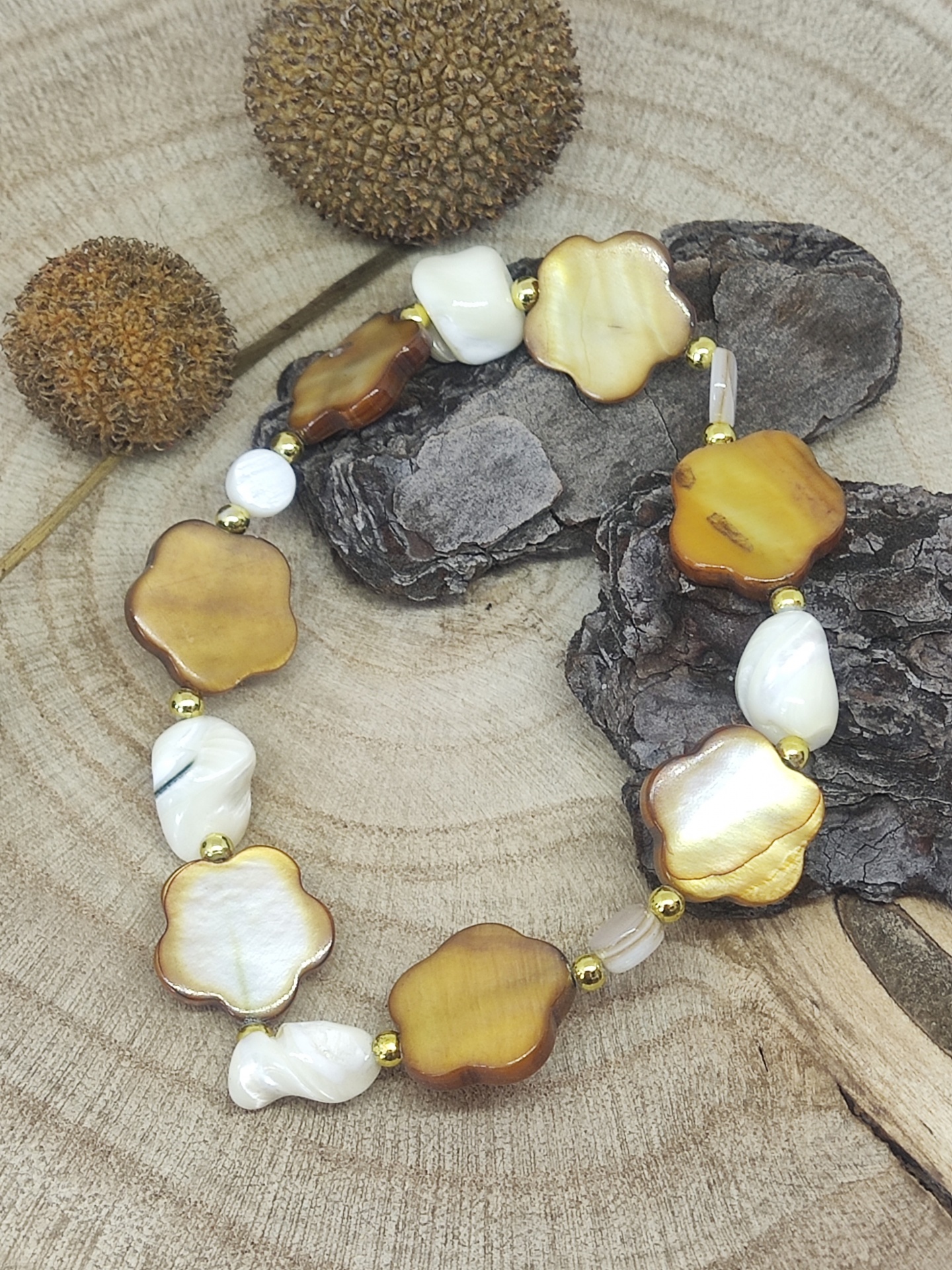 Pulseira de madrepérola em forma de flor com contas douradas sobre base de madeira