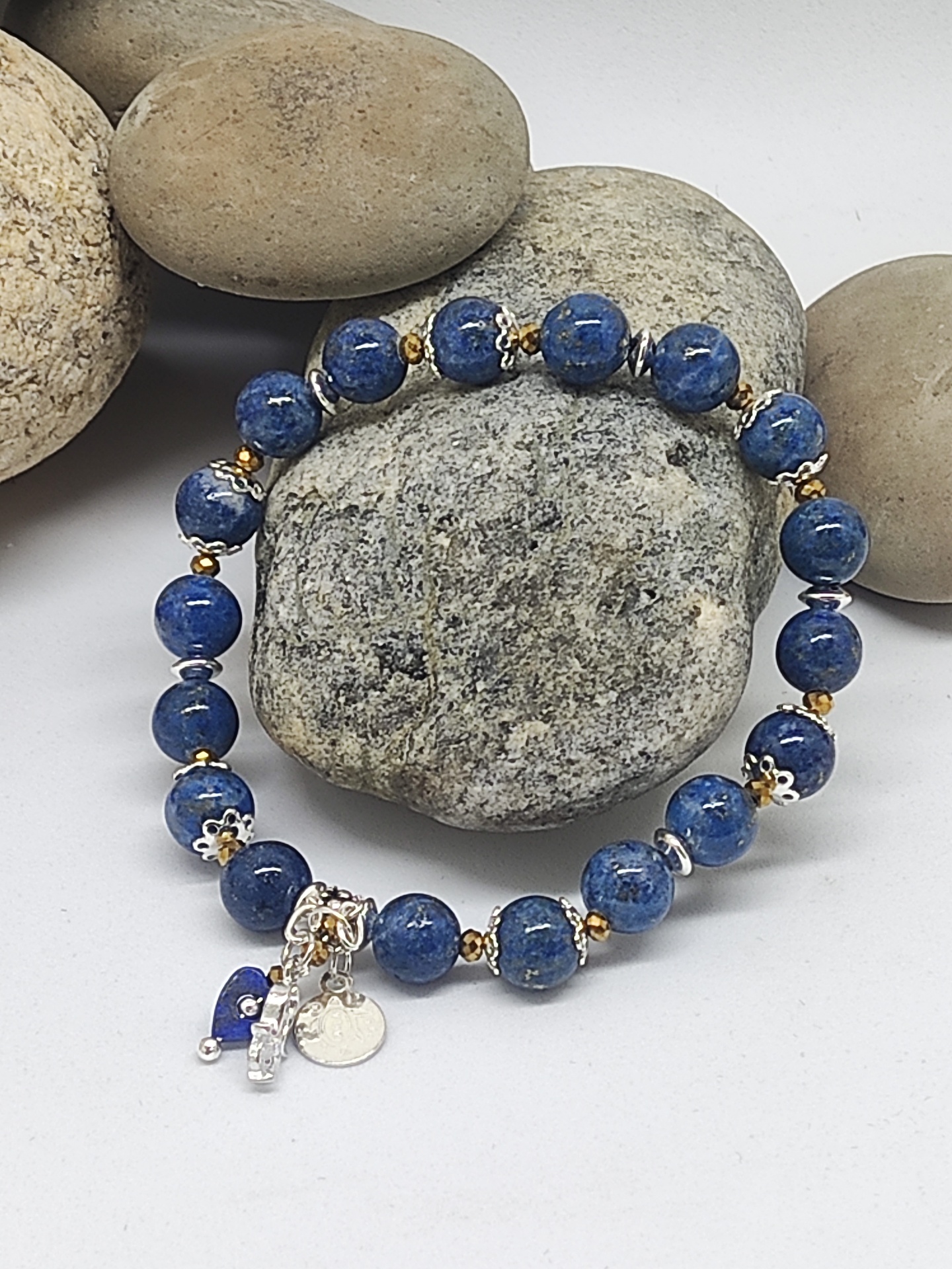 Pulseira de contas azuis com detalhes metálicos sobre pedras cinzentas e castanhas