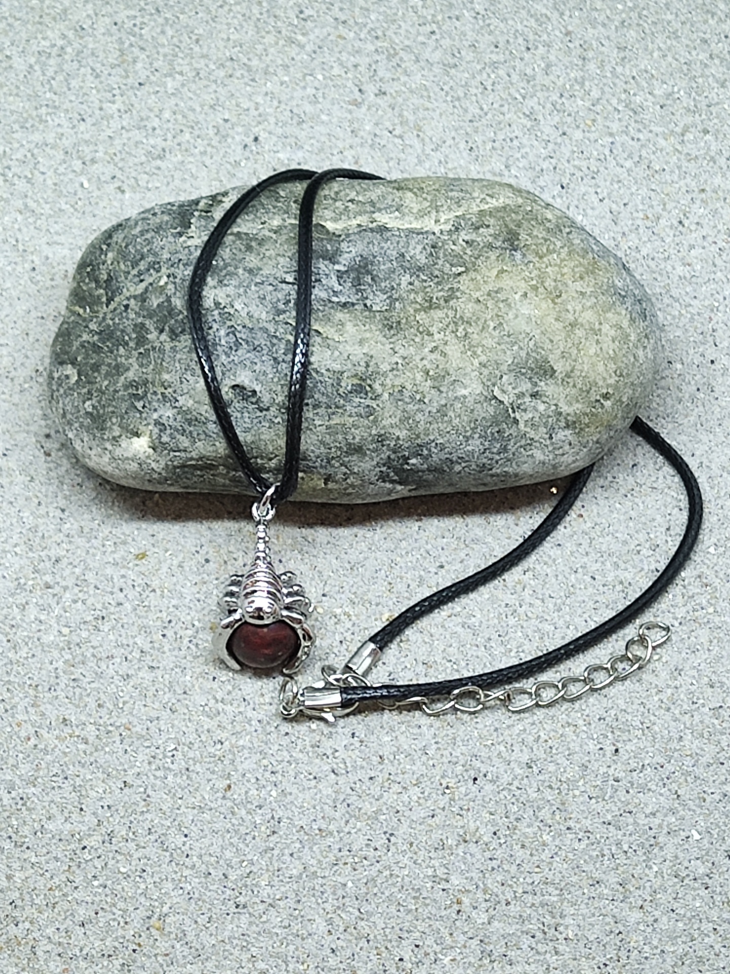 Colar com cordão preto e pendente prateado com pedra vermelha sobre pedra cinzenta