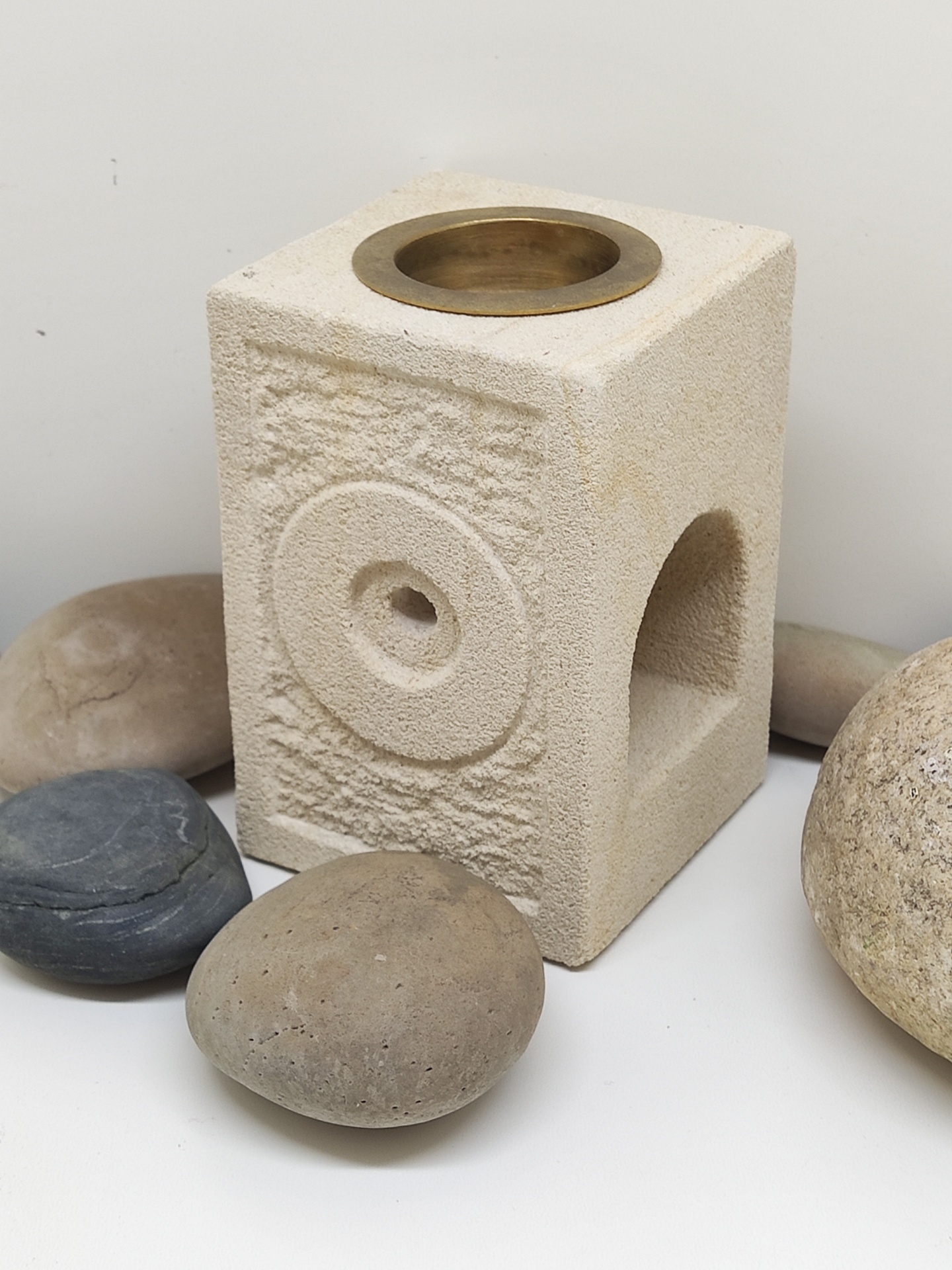 Queimador de óleo essencial de pedra bege com cavidade metálica dourada no topo rodeado por pedras