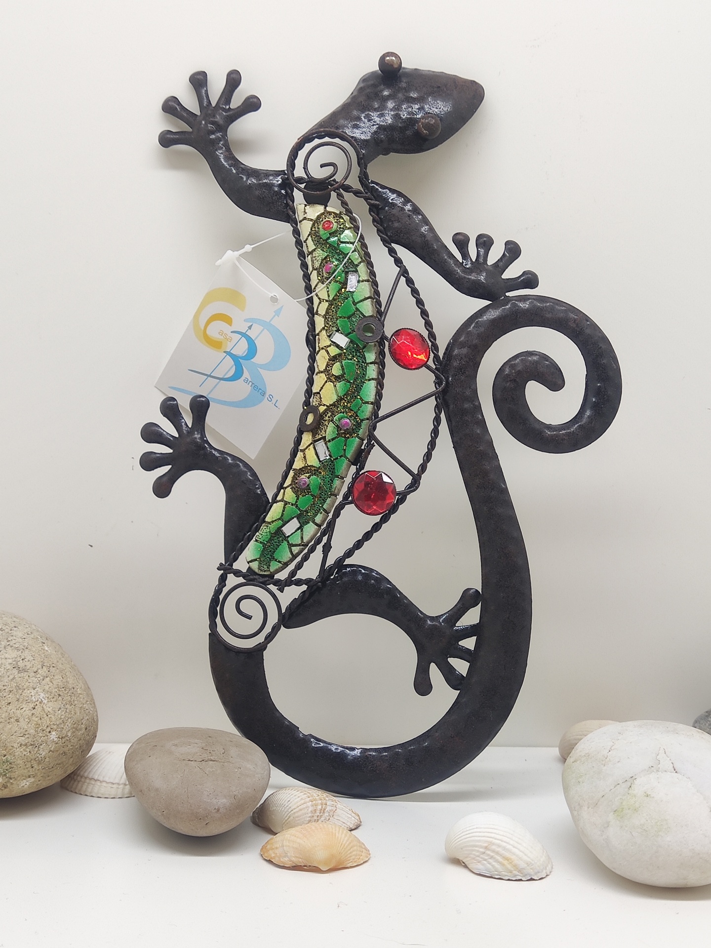 Escultura metálica de lagarto com mosaico verde e vermelho junto a pedras e conchas