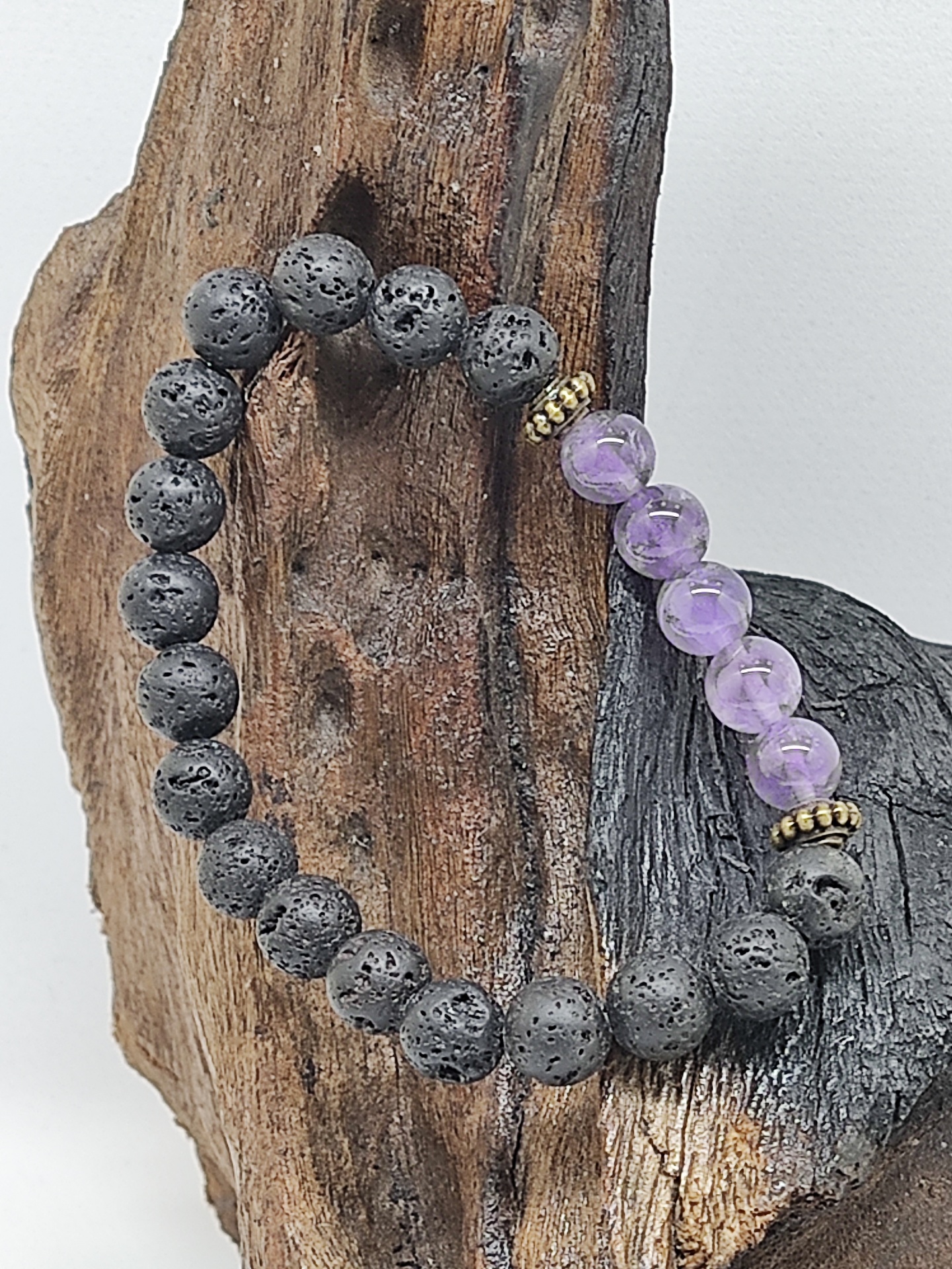 Pulseira de contas pretas vulcânicas e roxas ametista sobre suporte de madeira rústica