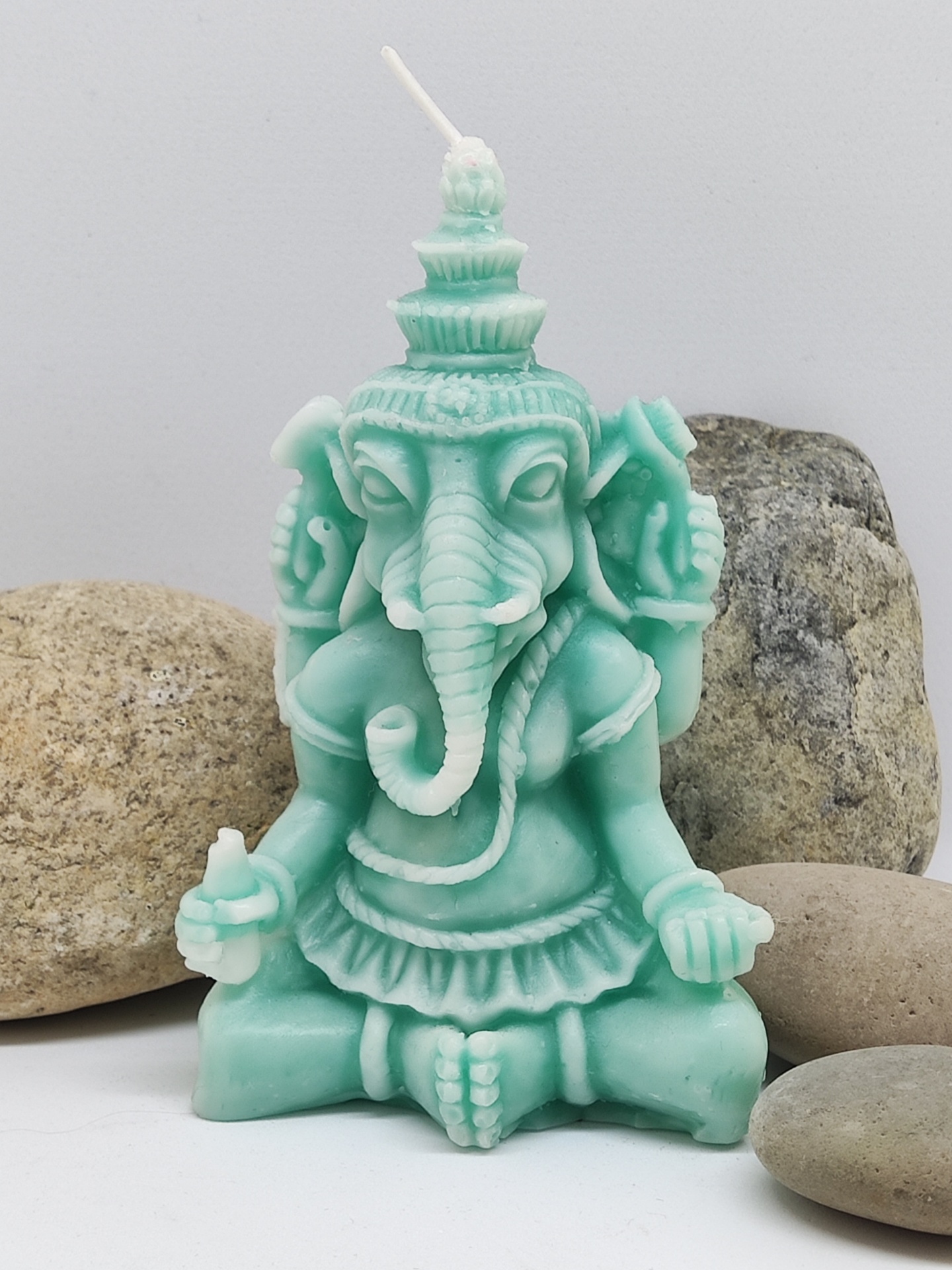 Vela verde em forma de Ganesha sentado com quatro braços e pavio no topo, rodeada por pedras.