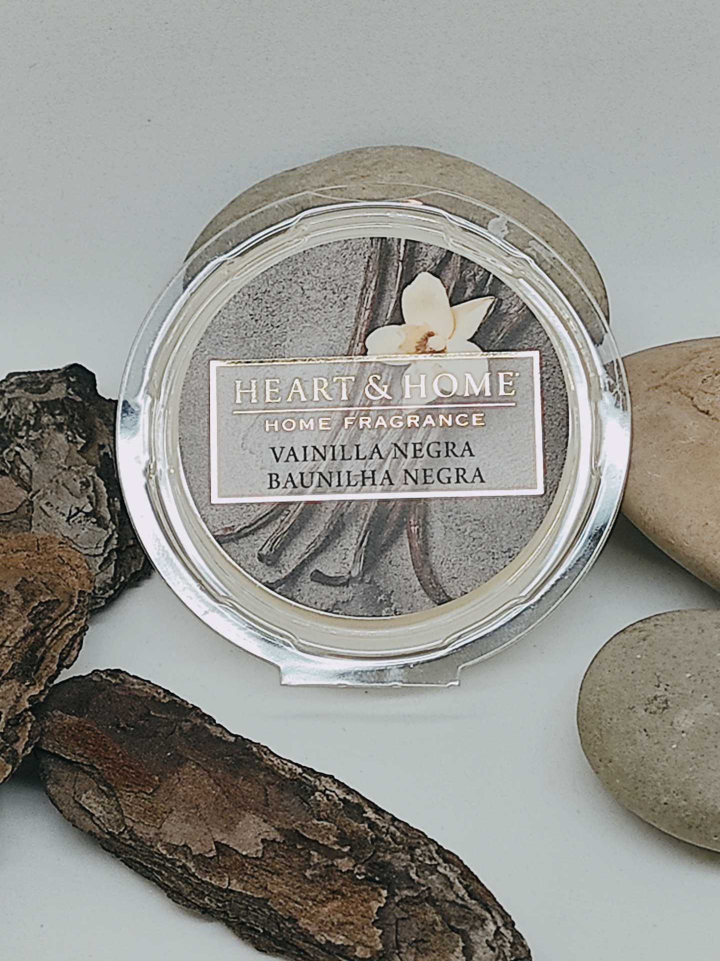 Frasco redondo transparente de fragrância para casa HEART & HOME com aroma baunilha negra, rodeado por pedras e casca de árvore