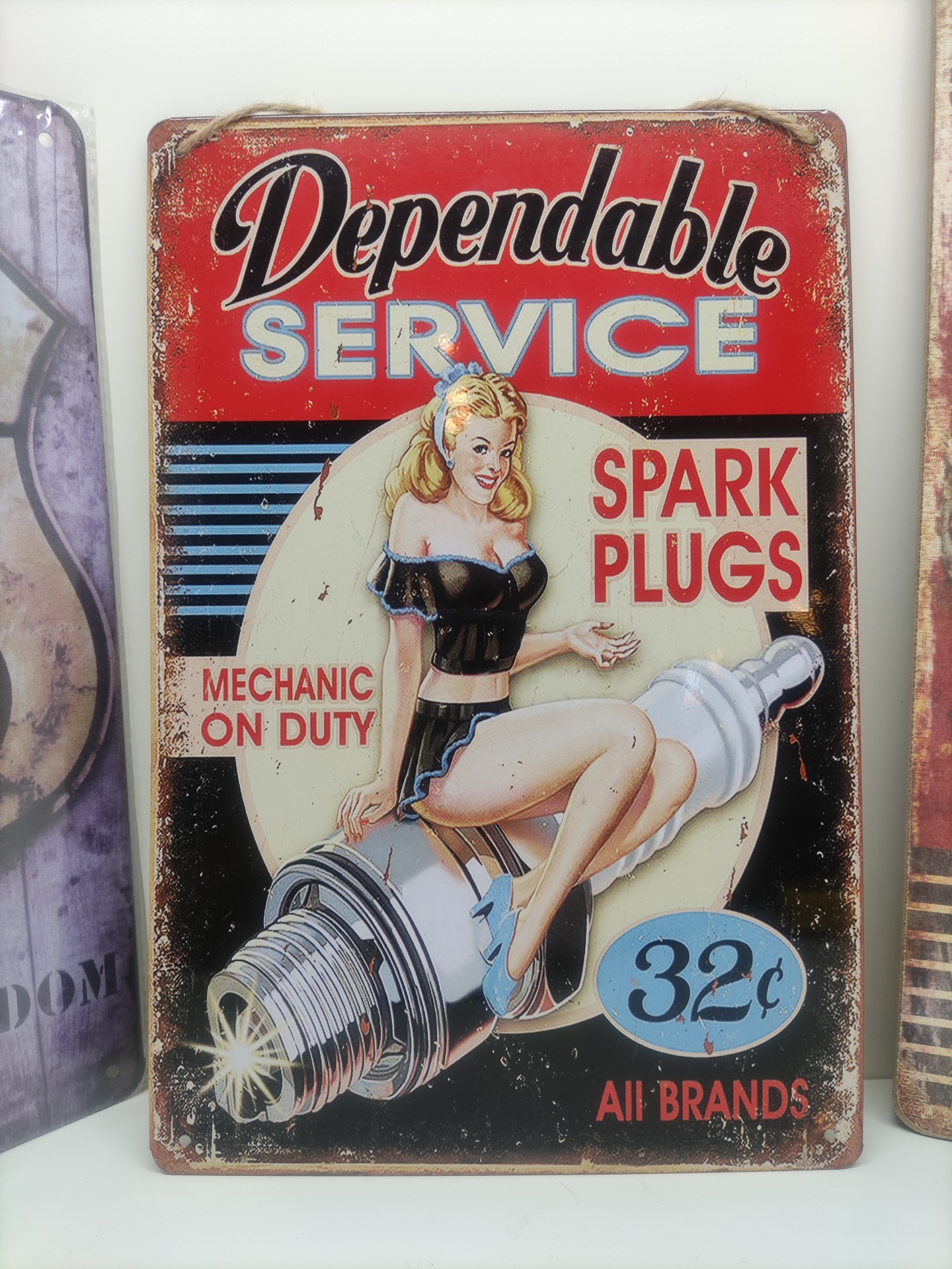 Placa metálica vintage com mulher pin-up e texto publicitário de velas de ignição.